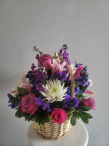 Basket arrangement of pink roses, white lilies, and purple flowers