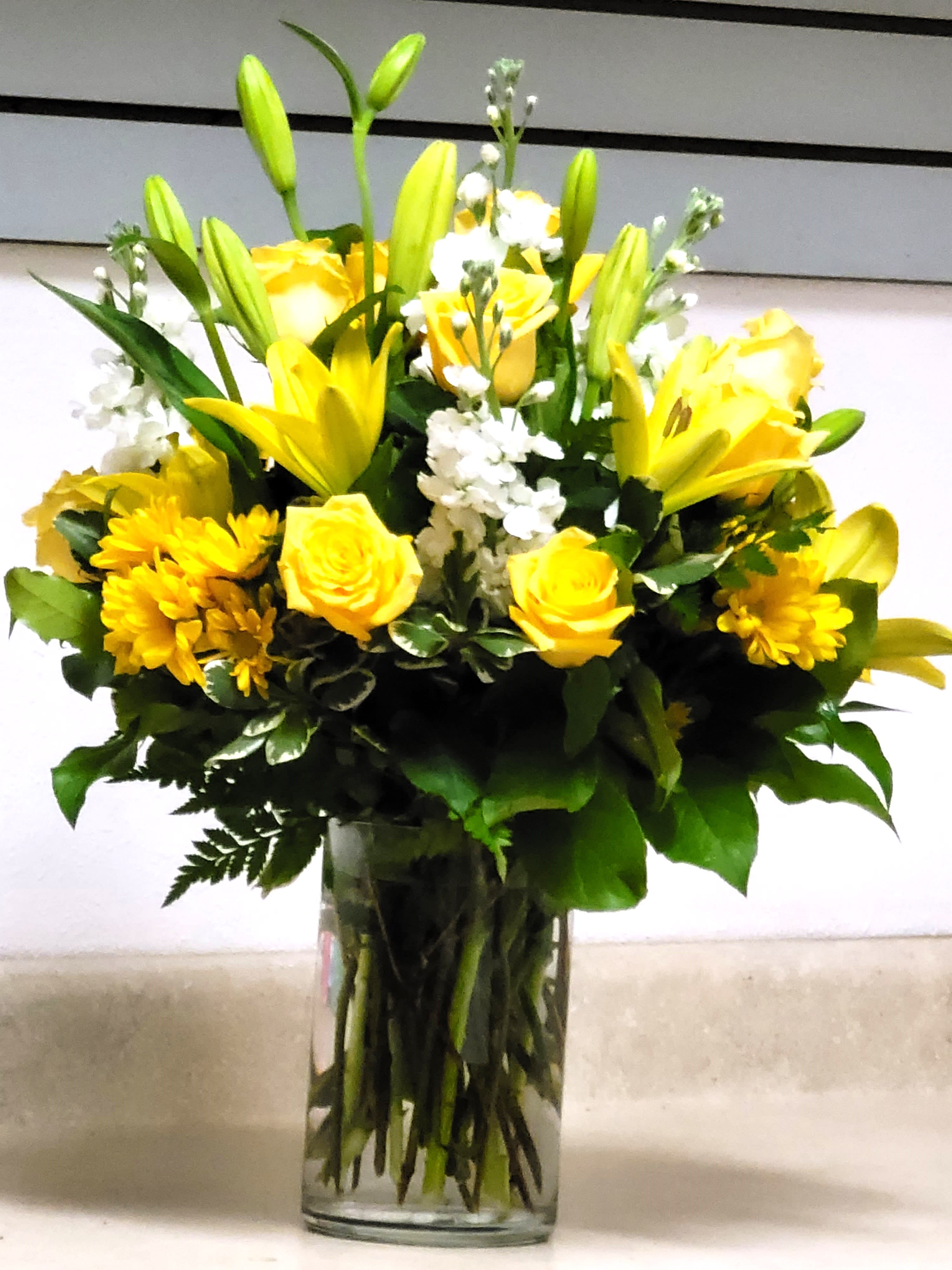 Yellow roses and lilies arranged in a clear glass vase