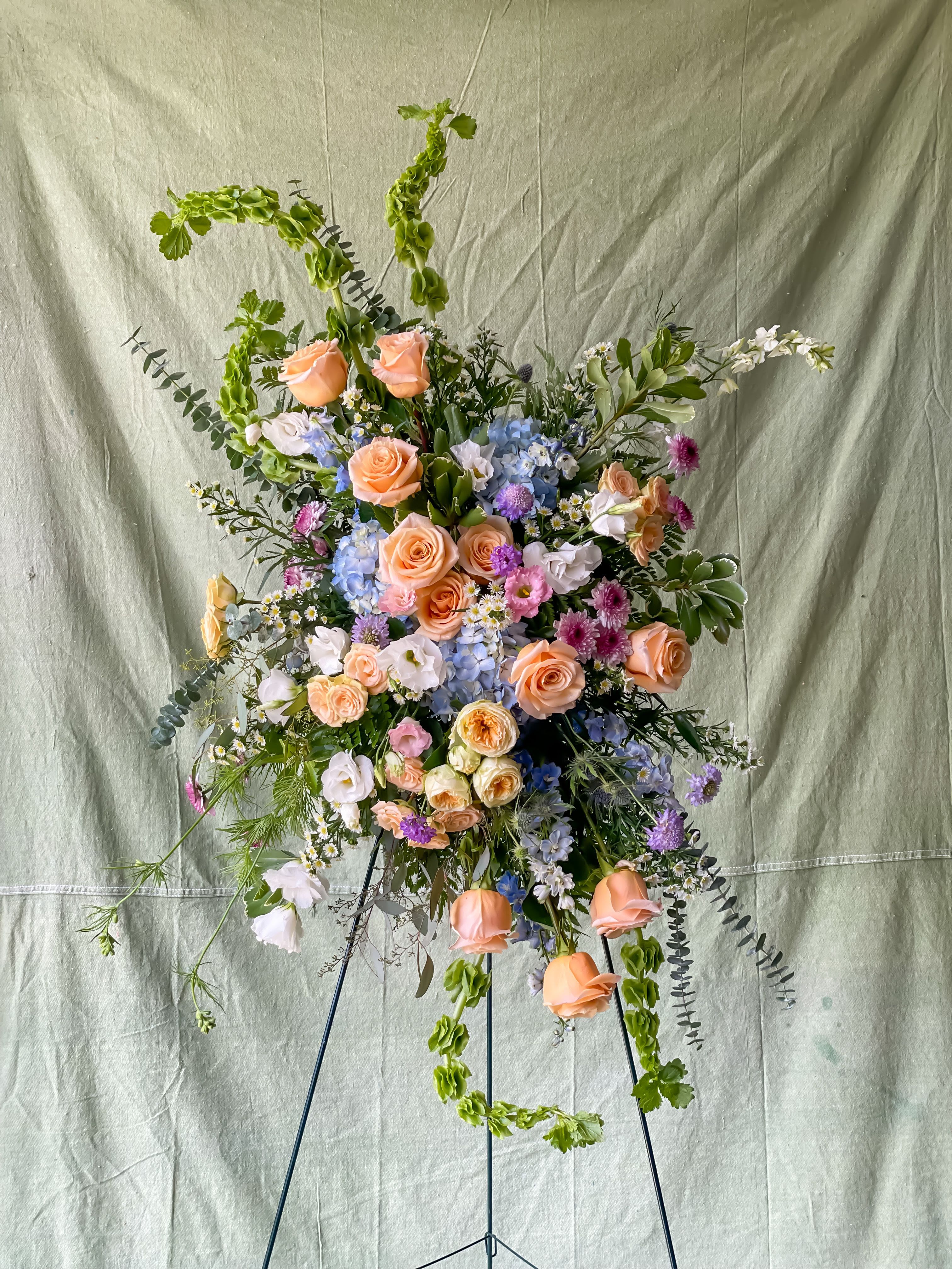 Tall floral spray with peach roses, blue hydrangea, and purple accents on a stand