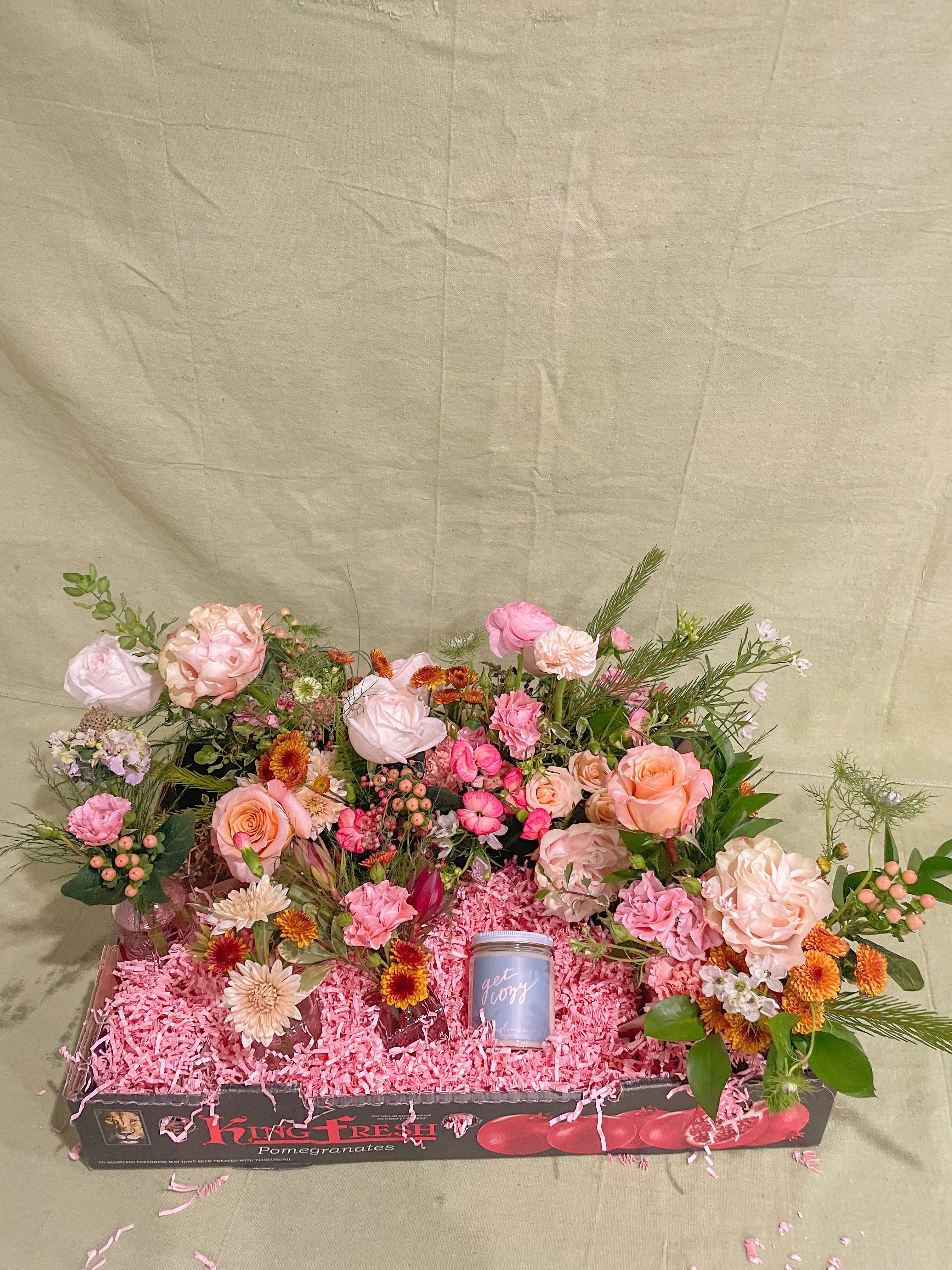 Mixed pink and peach flower arrangement in a gift box with a small candle
