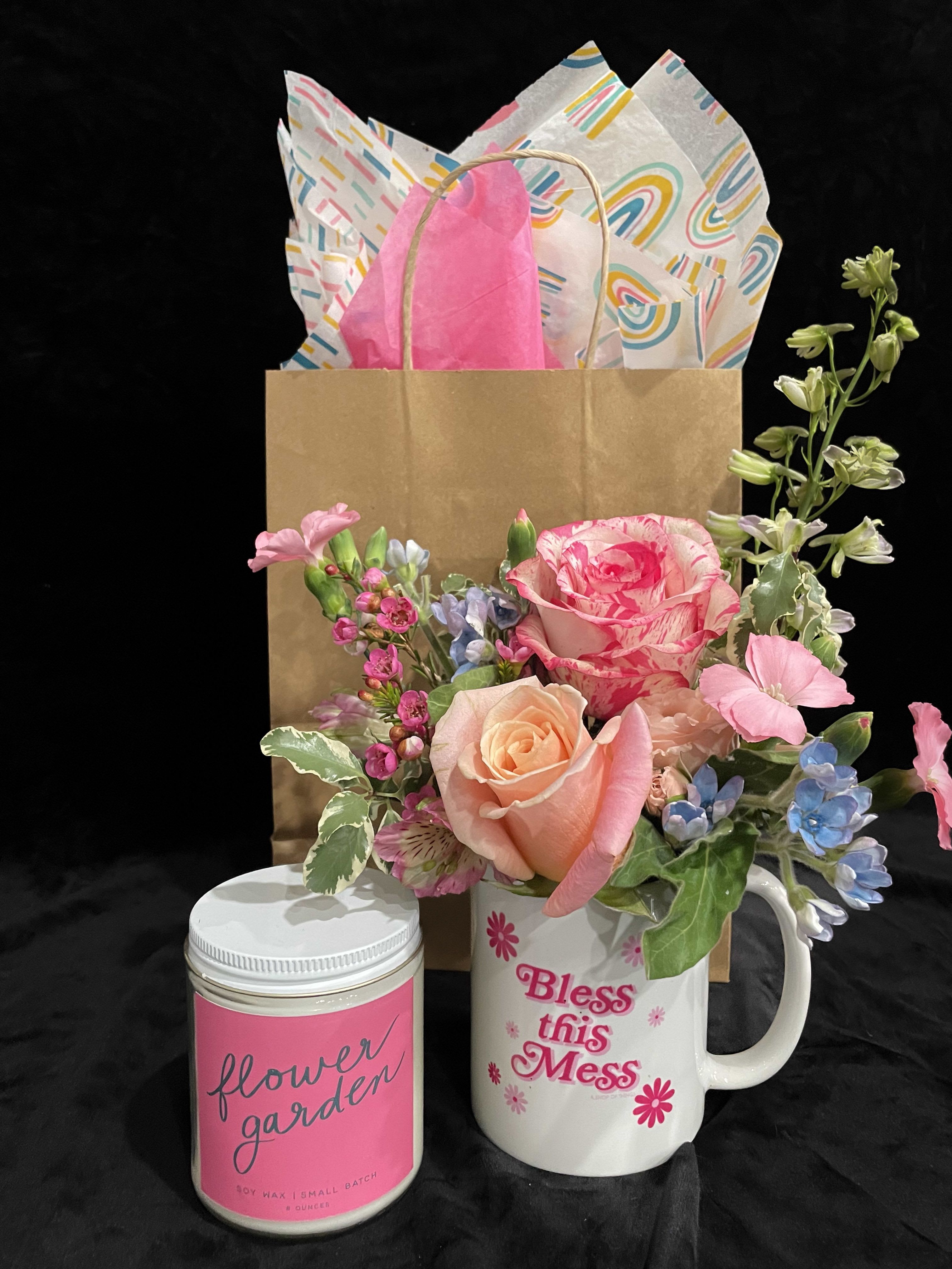 Pink and peach flower arrangement in a white mug with a candle and gift bag