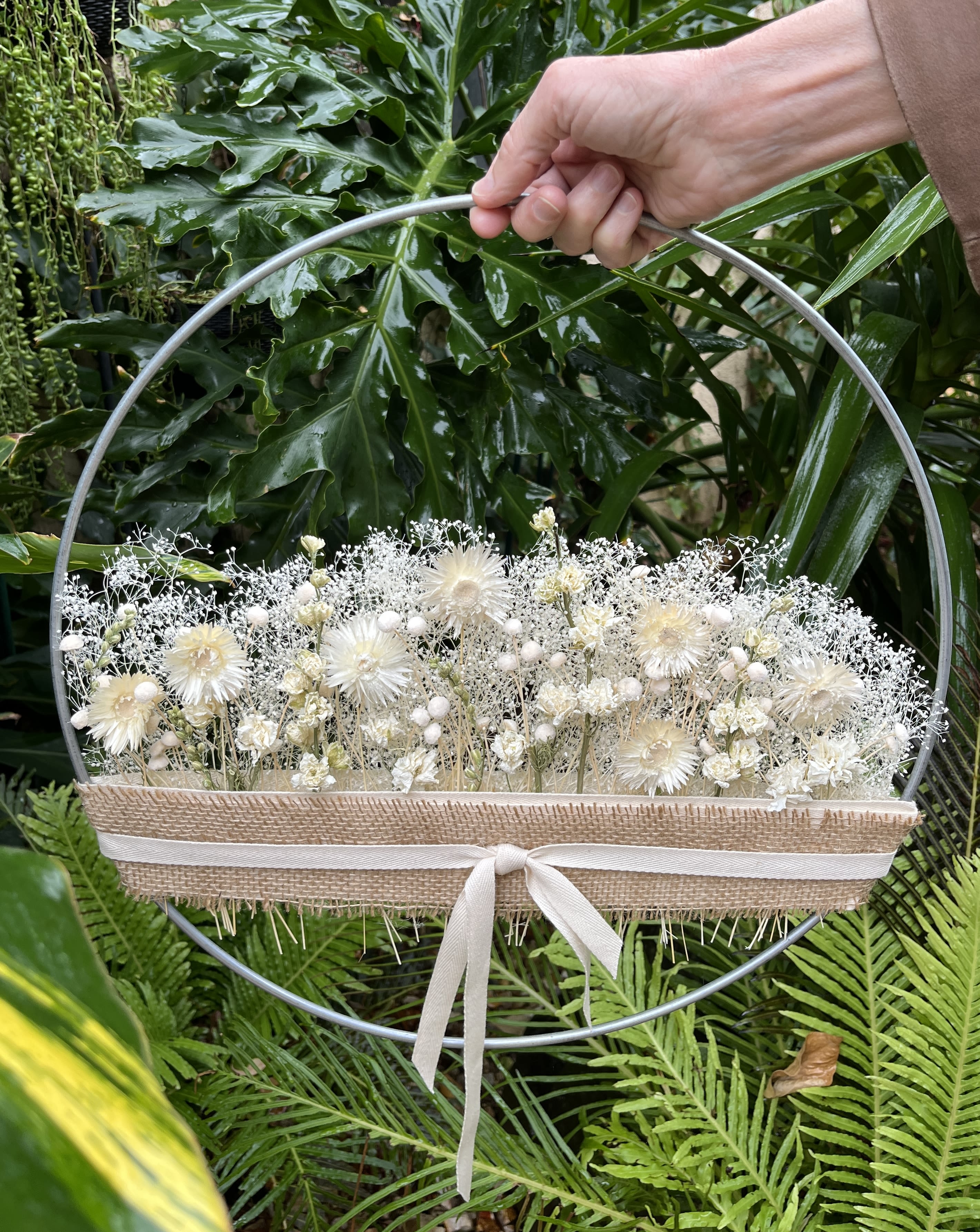 White floral arrangement in a round metal hoop with a ribbon-tied burlap wrap