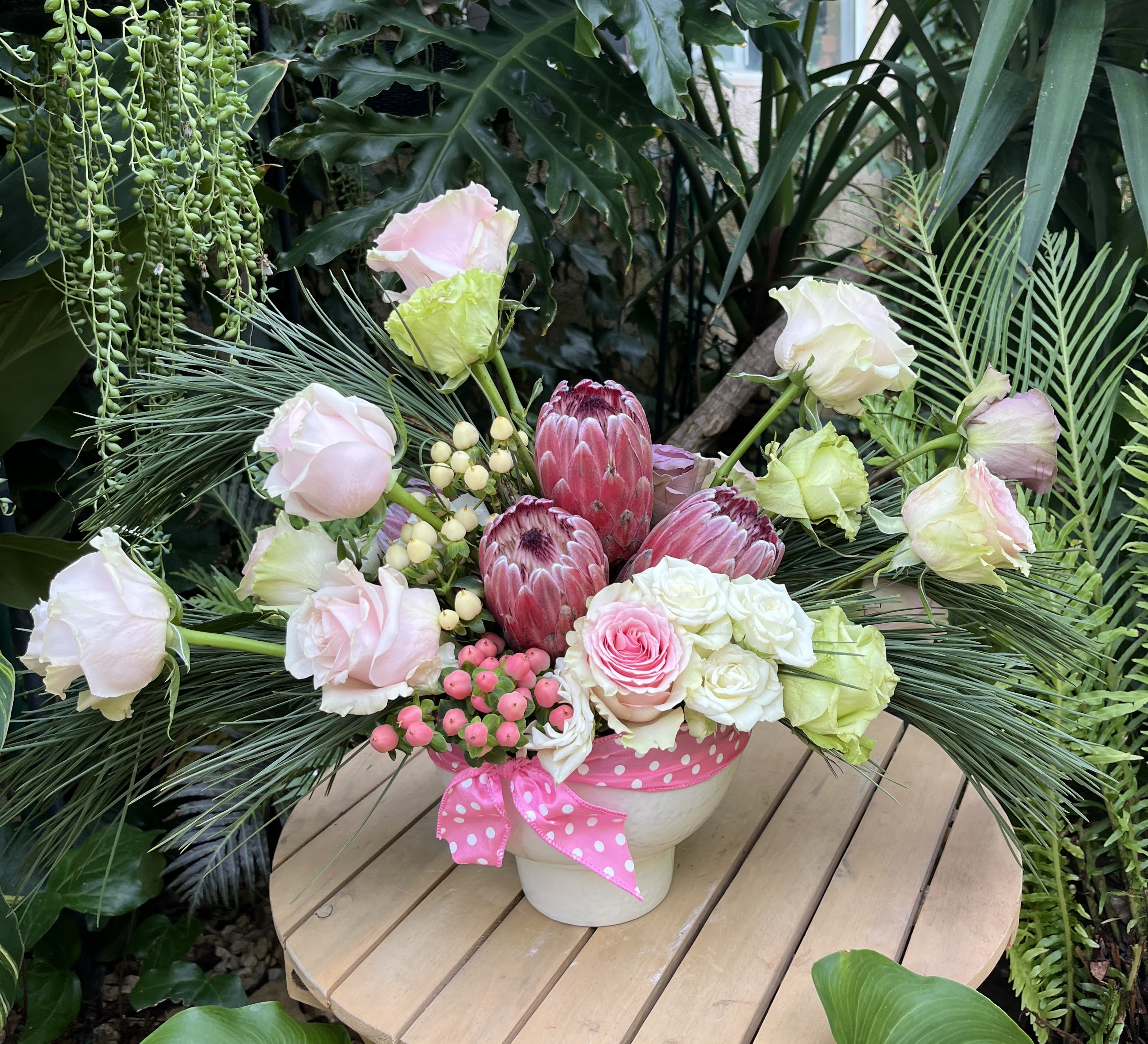 Pink and white floral arrangement in a white pot with a pink ribbon