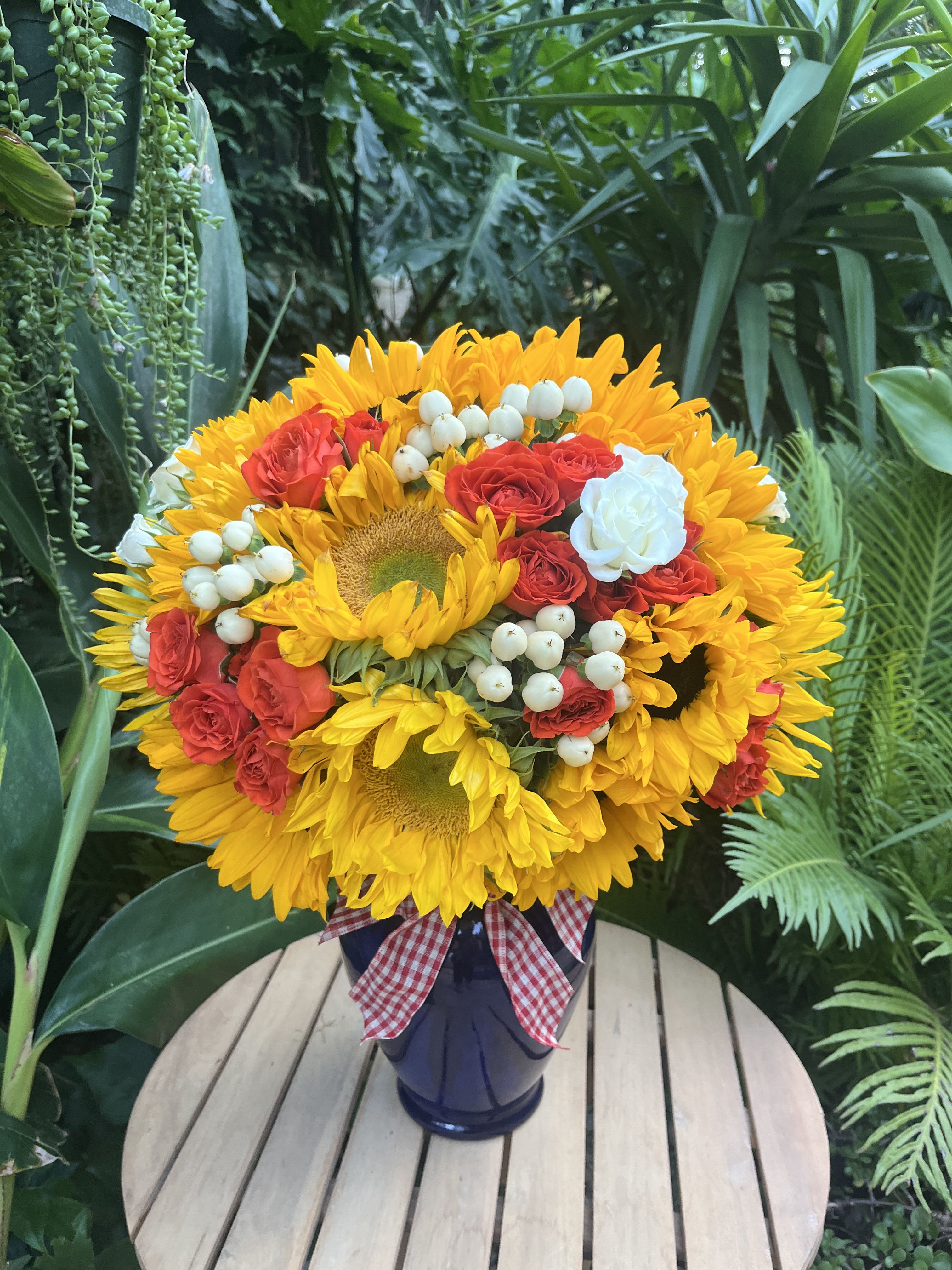 Sunflower and red rose bouquet in a dark vase with a gingham ribbon