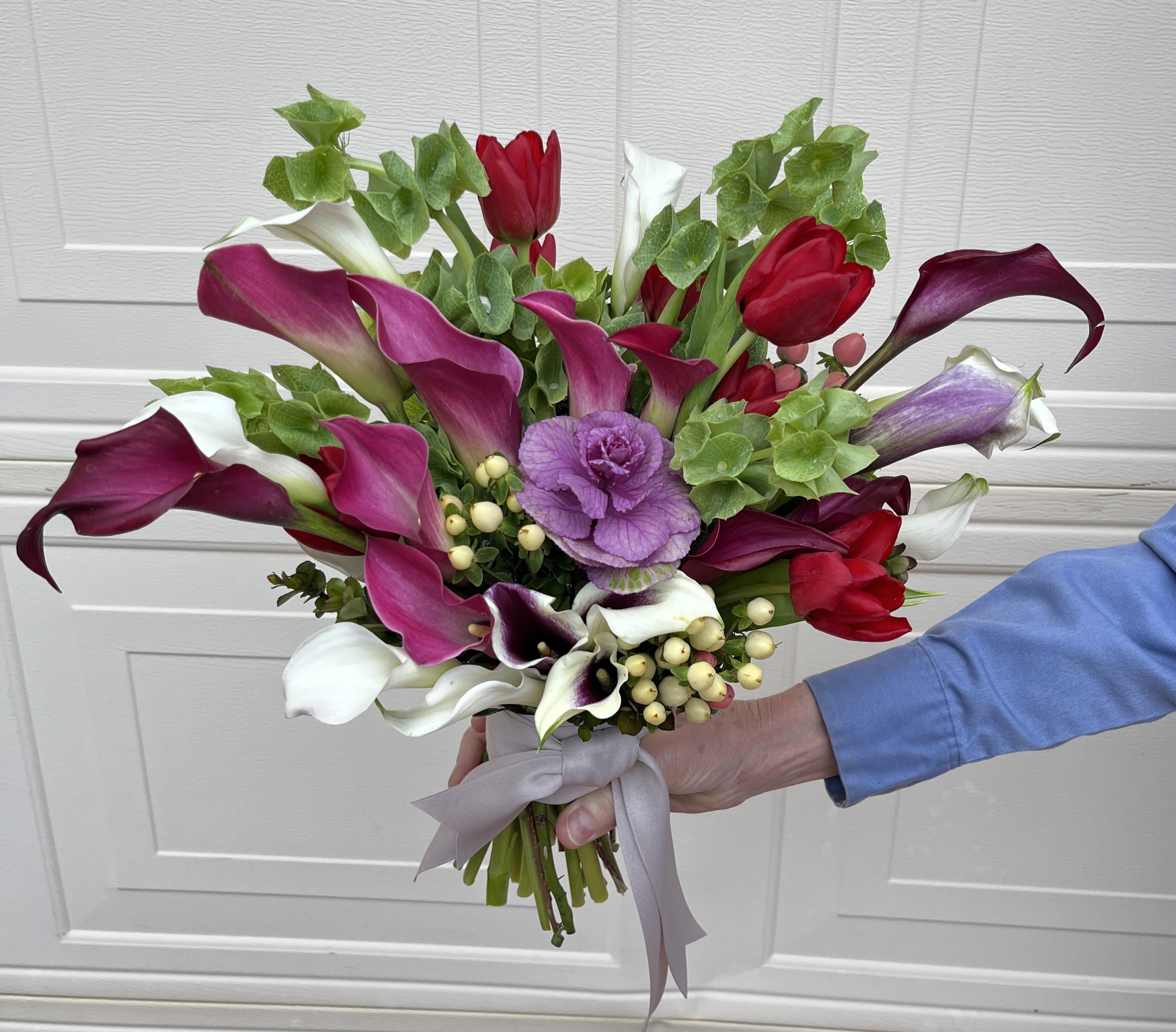 Handheld bouquet of calla lilies and tulips in pink, white, and red