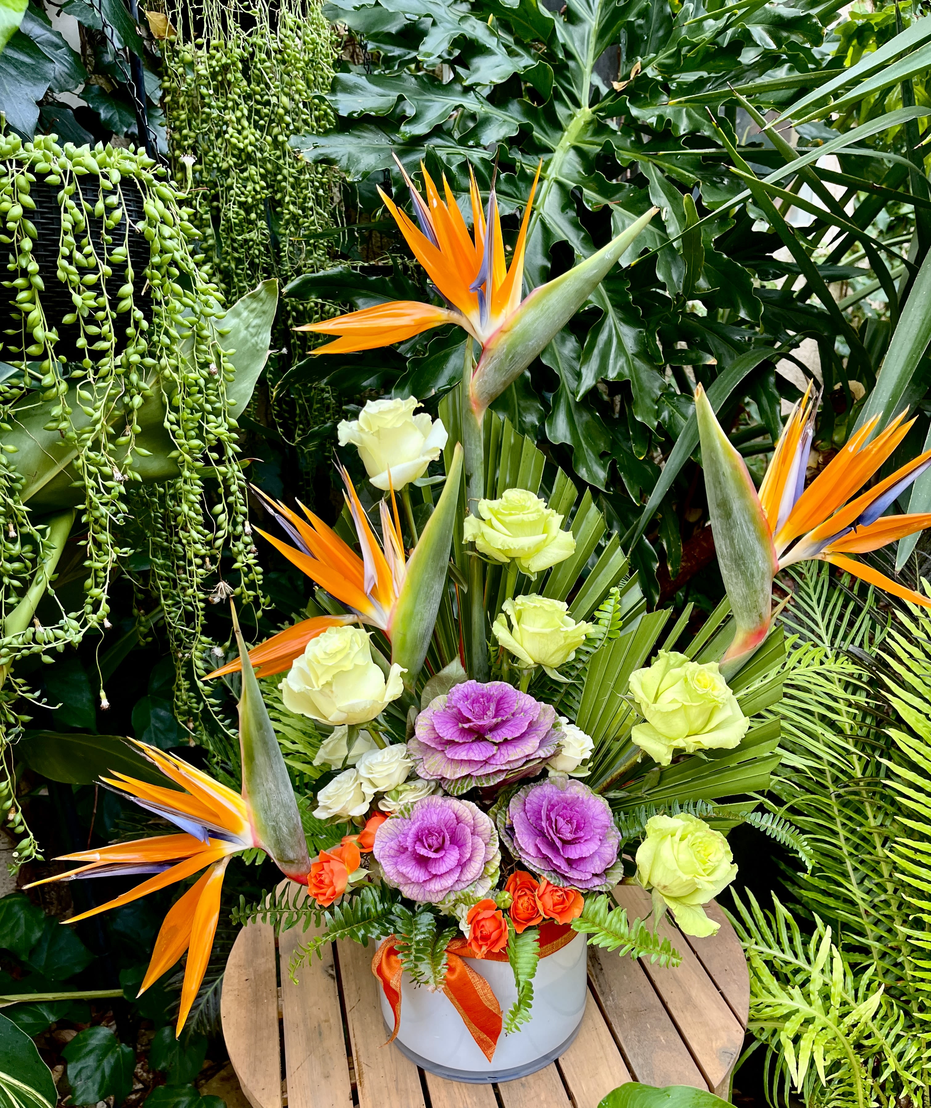 Tropical floral arrangement with orange bird of paradise and purple flowers in a white container