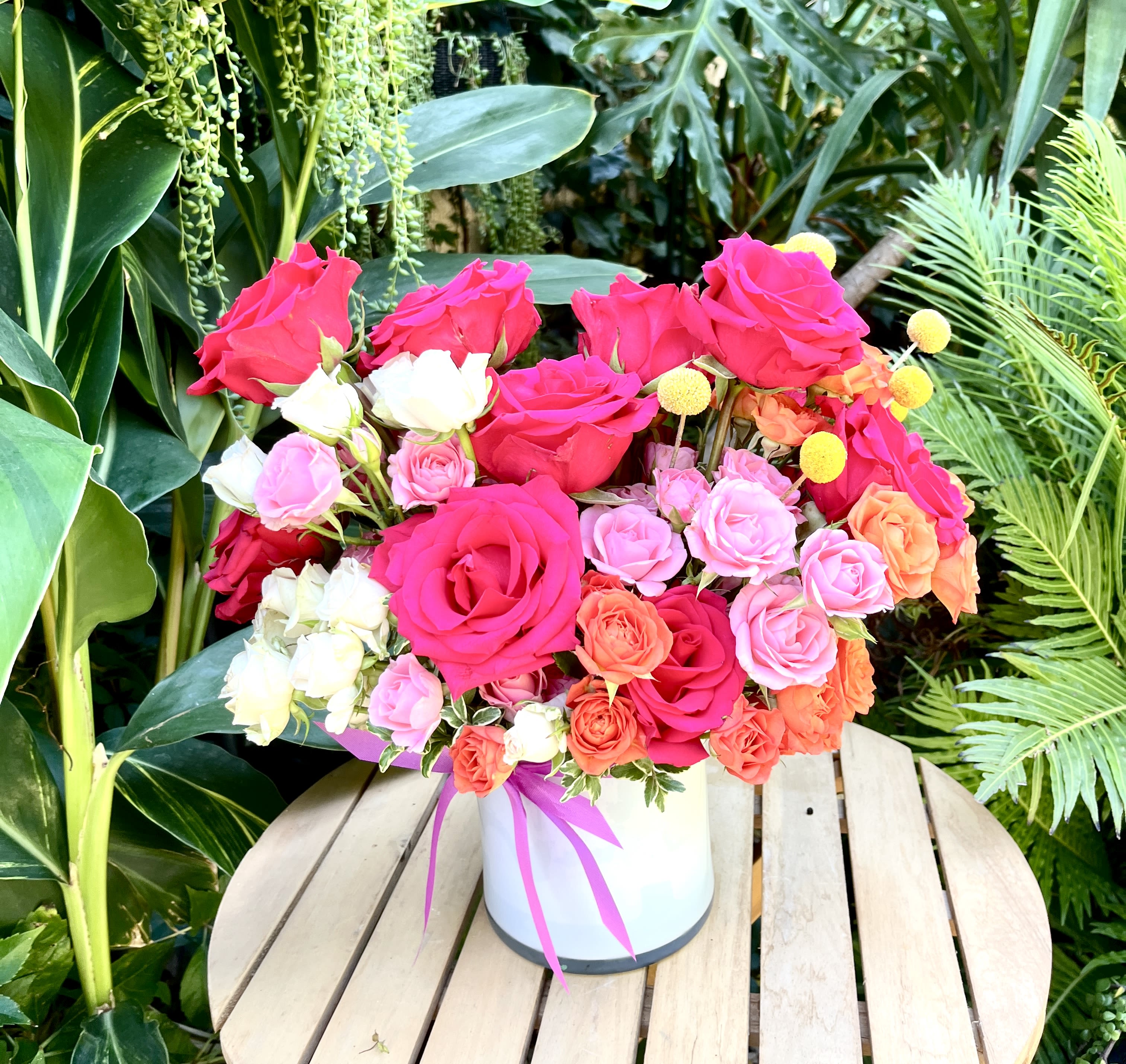 Bright mixed roses arranged in a white hatbox with a pink ribbon