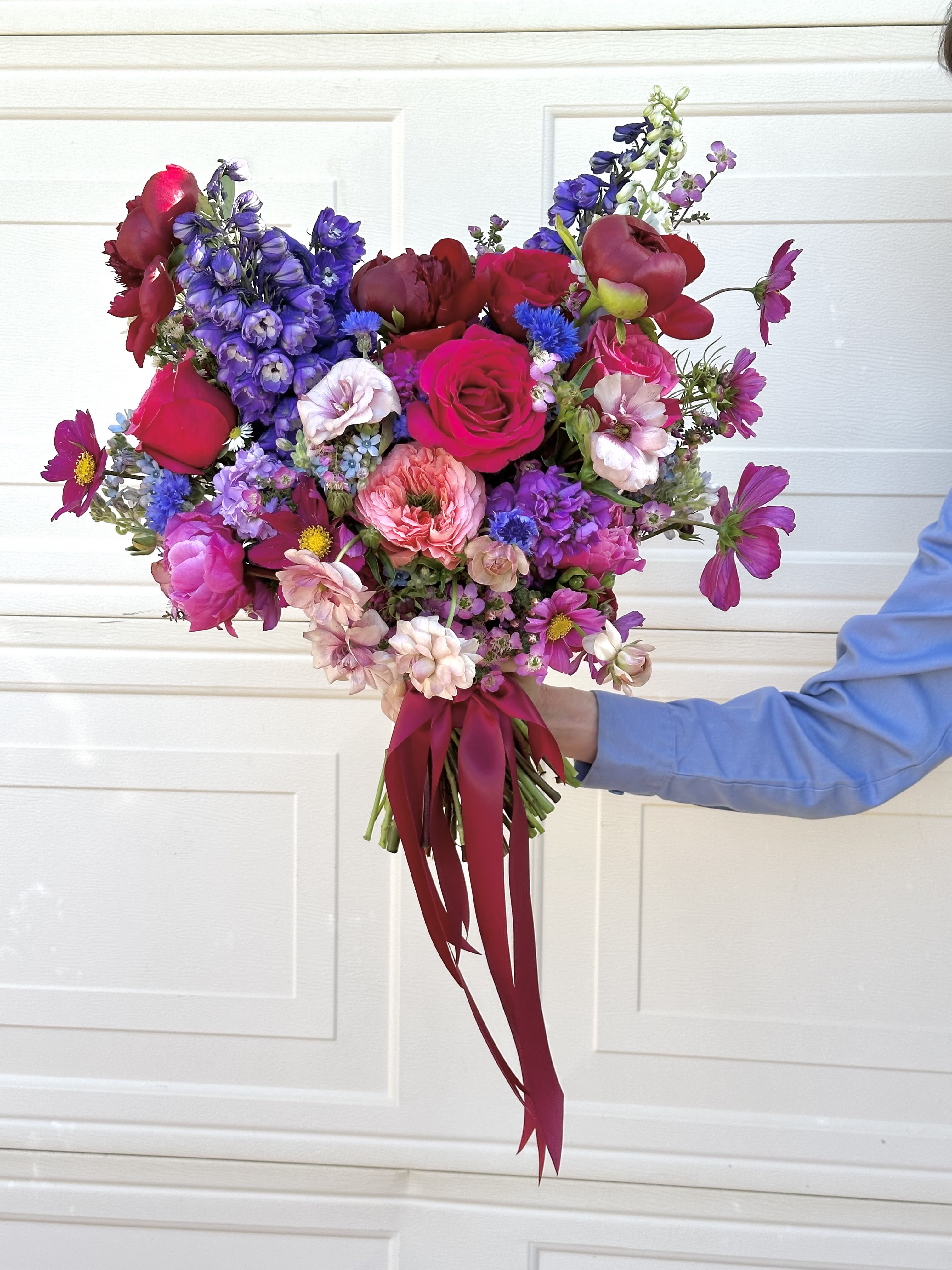 Handheld bouquet of pink, red, and purple flowers tied with a burgundy ribbon.