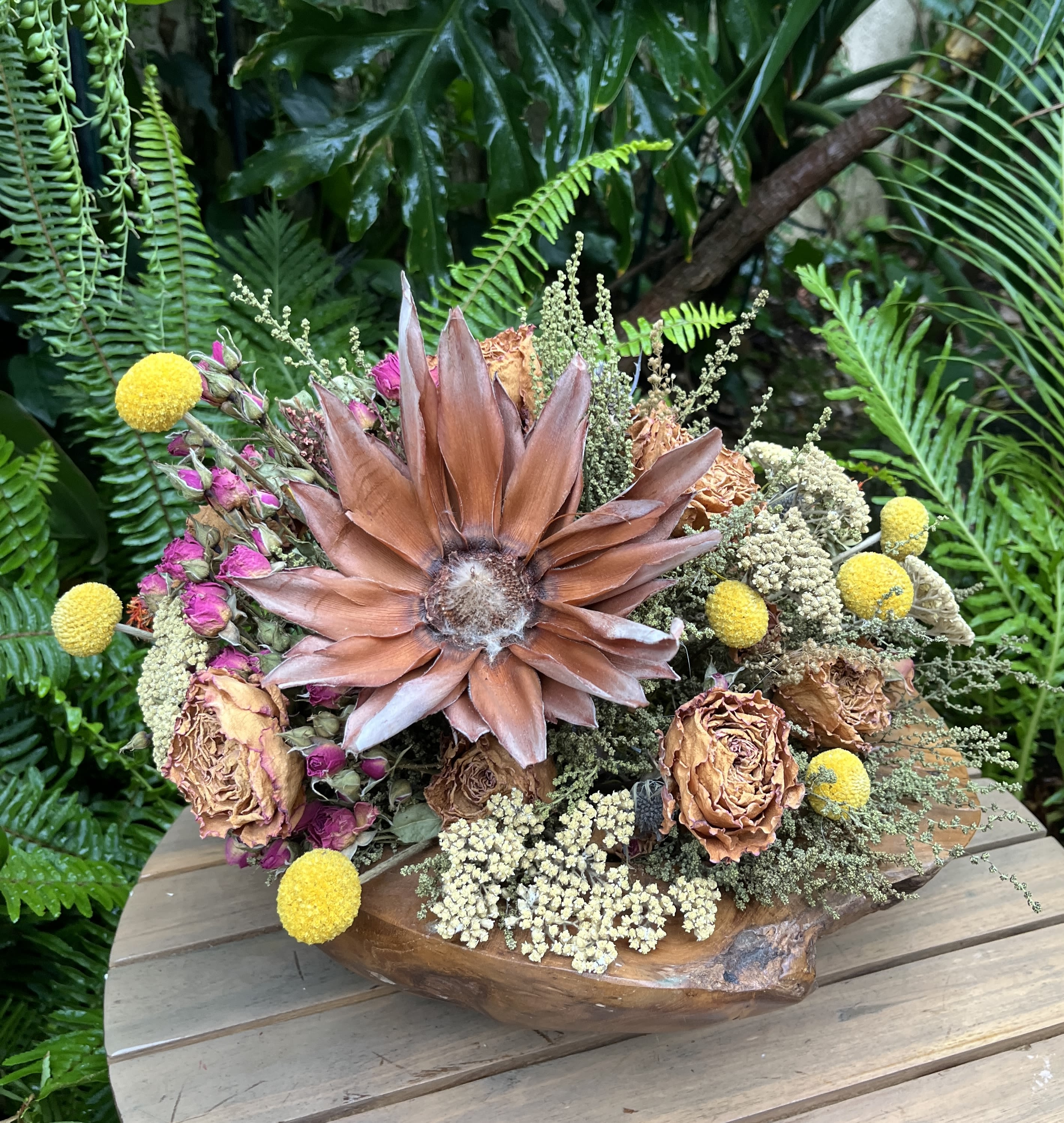 Dried floral arrangement with a large copper-toned bloom in a wooden bowl