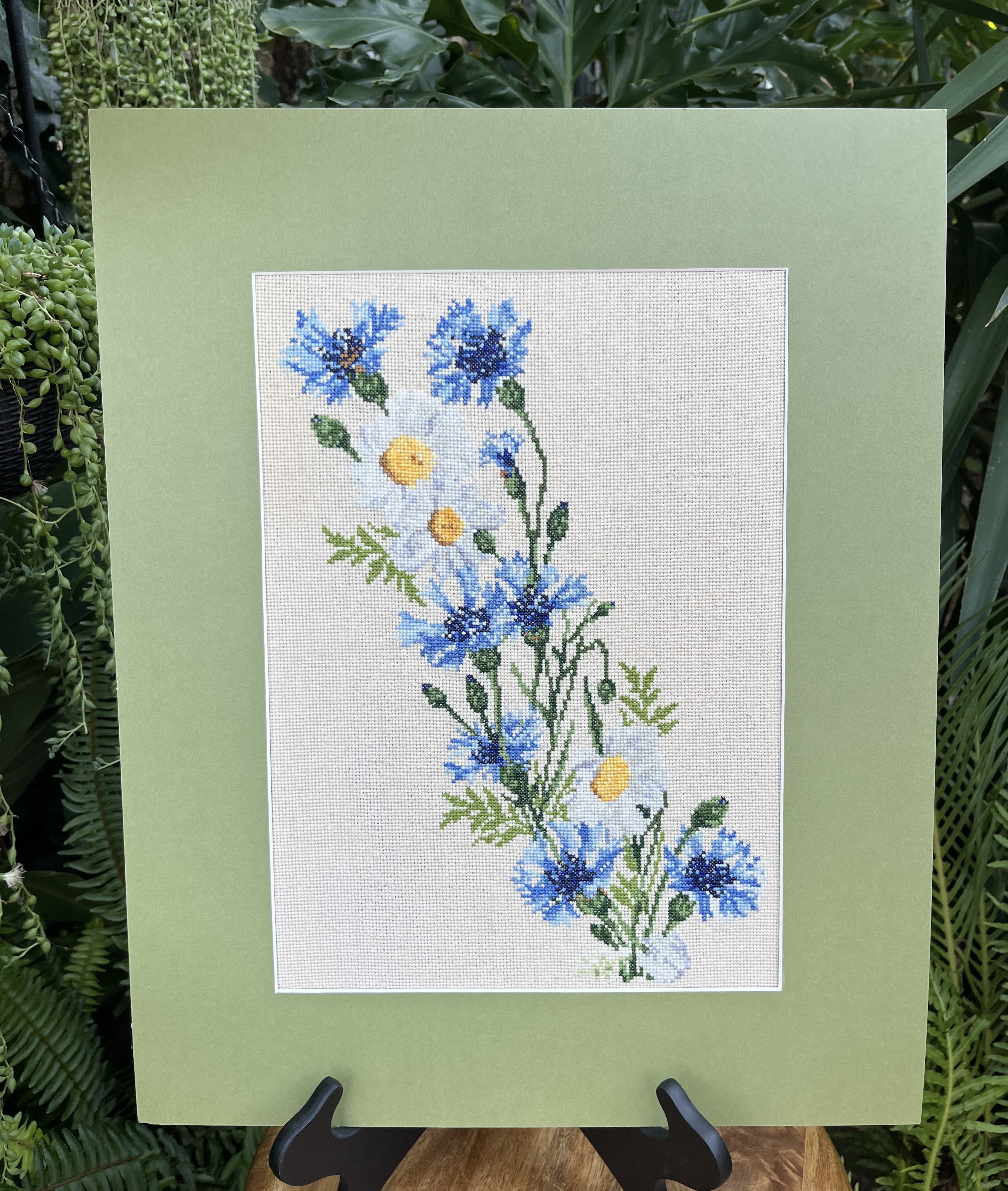 Framed floral embroidery with blue and white flowers on a pale green mat