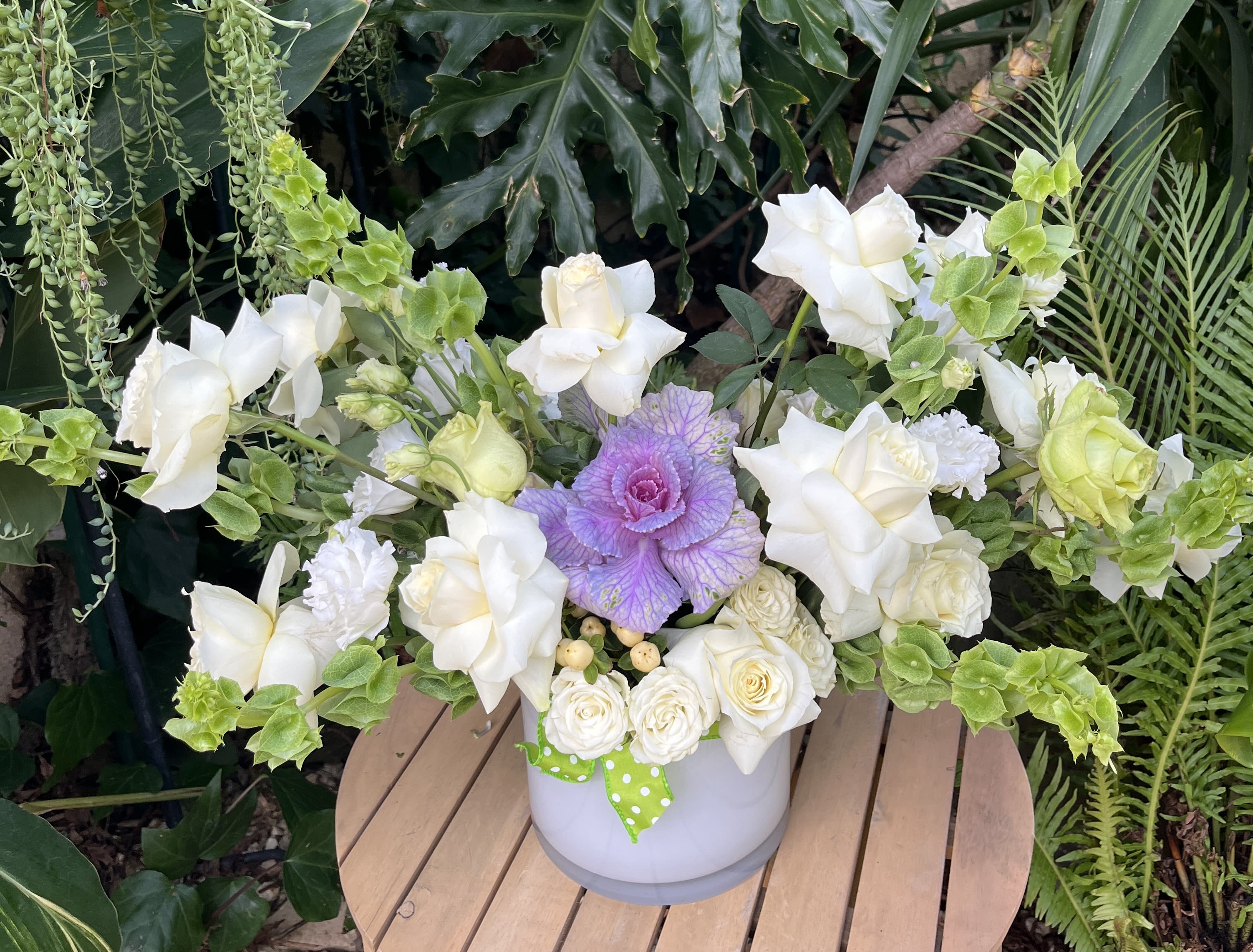 White roses and green snapdragons in a white vase with a purple cabbage center