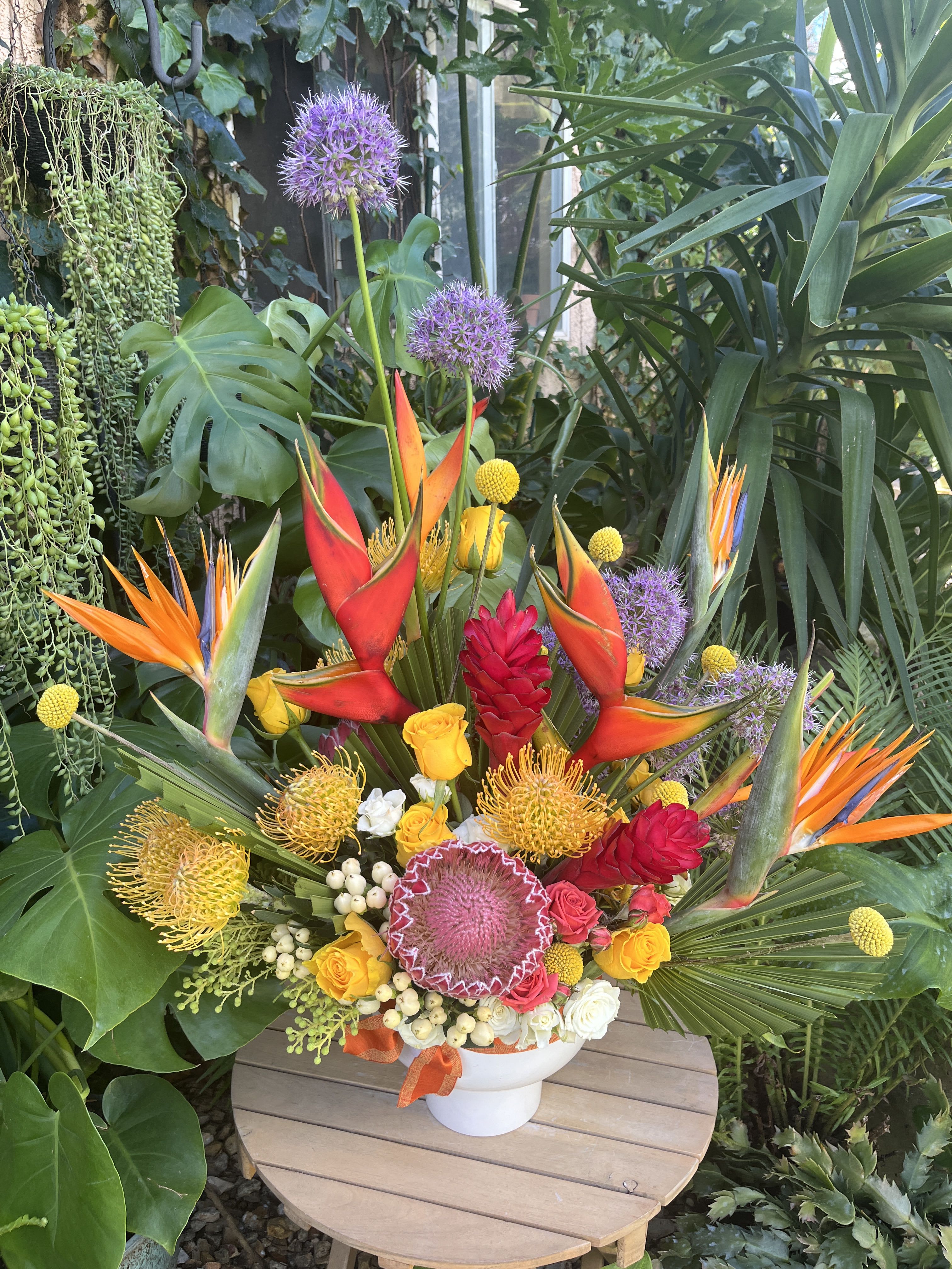 Tropical bouquet with bird of paradise, roses, and purple allium in a white vase