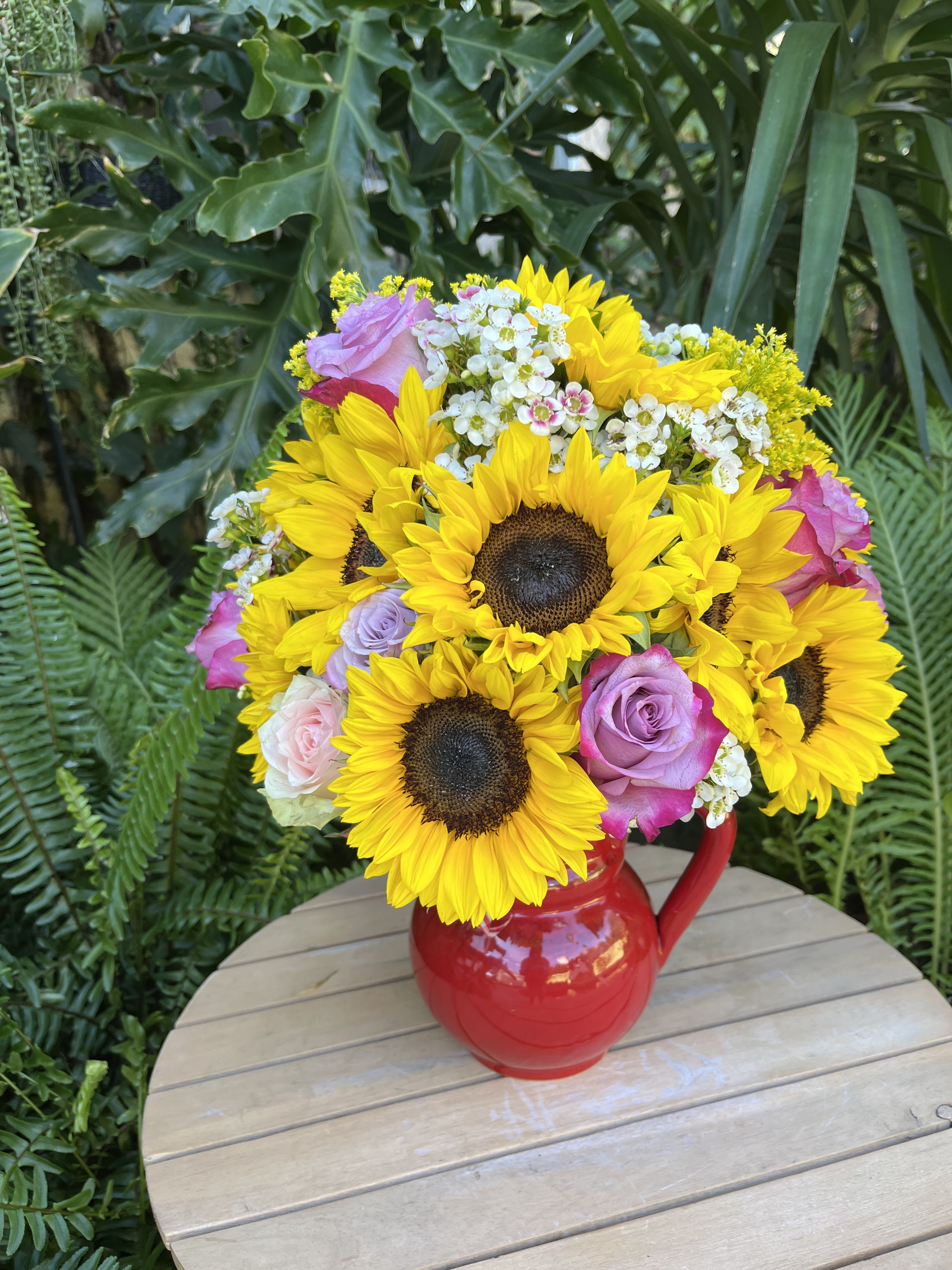 Bouquet of sunflowers and roses in a red pitcher vase