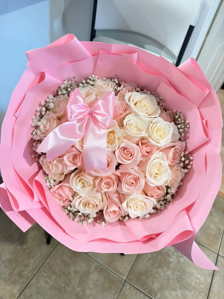 Pink-wrapped bouquet of pale pink and white roses with a satin bow
