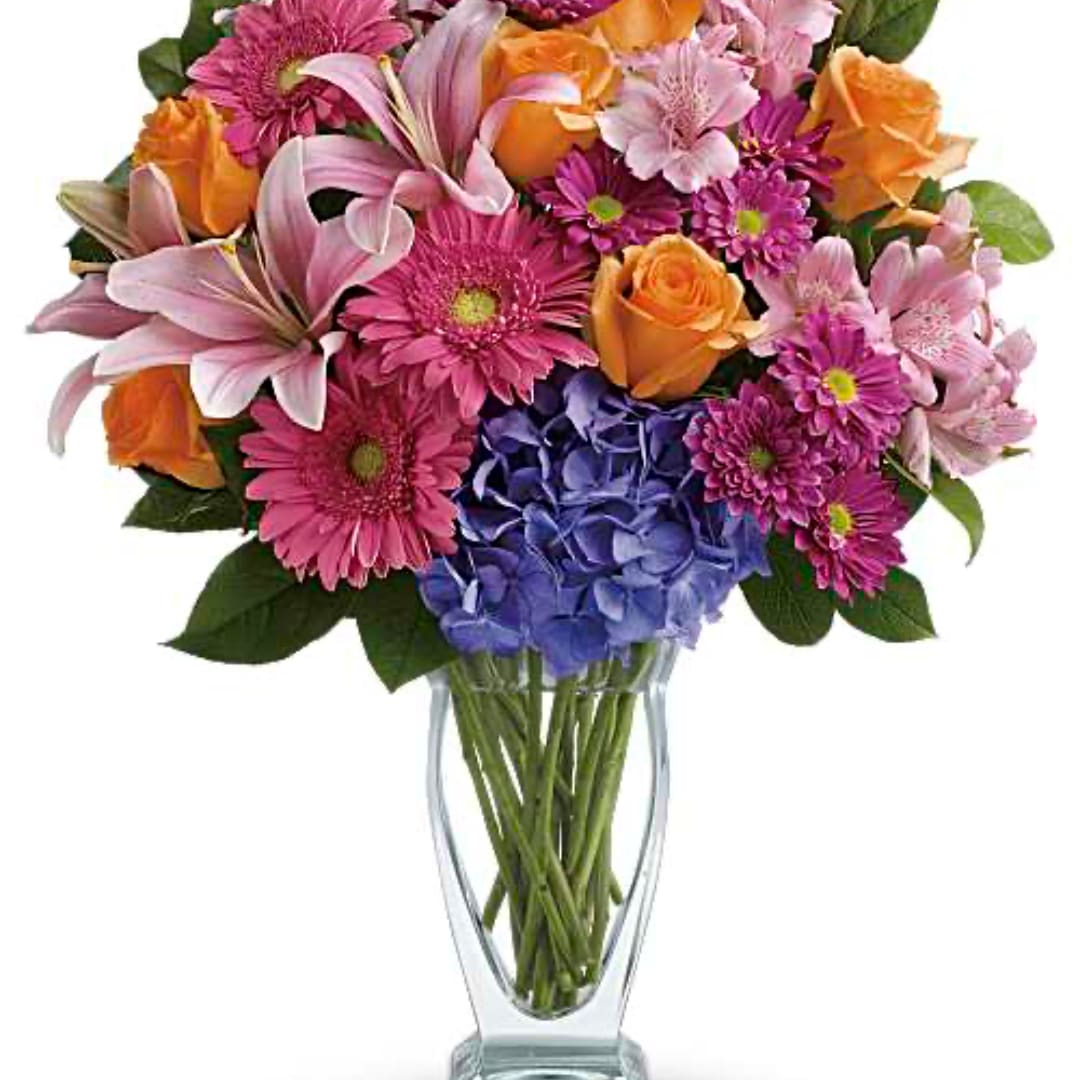 Mixed bouquet of pink, orange, and purple flowers in a clear glass vase