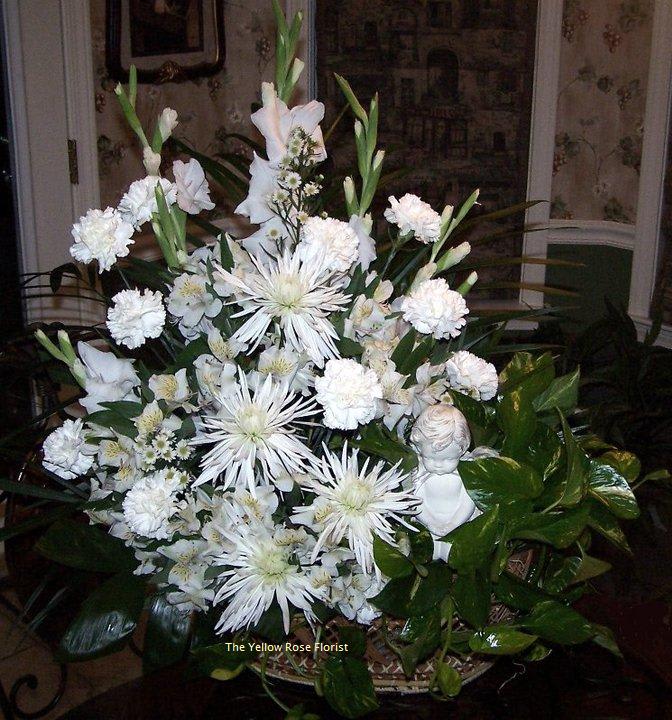 Large white floral arrangement in a basket with a small angel figurine