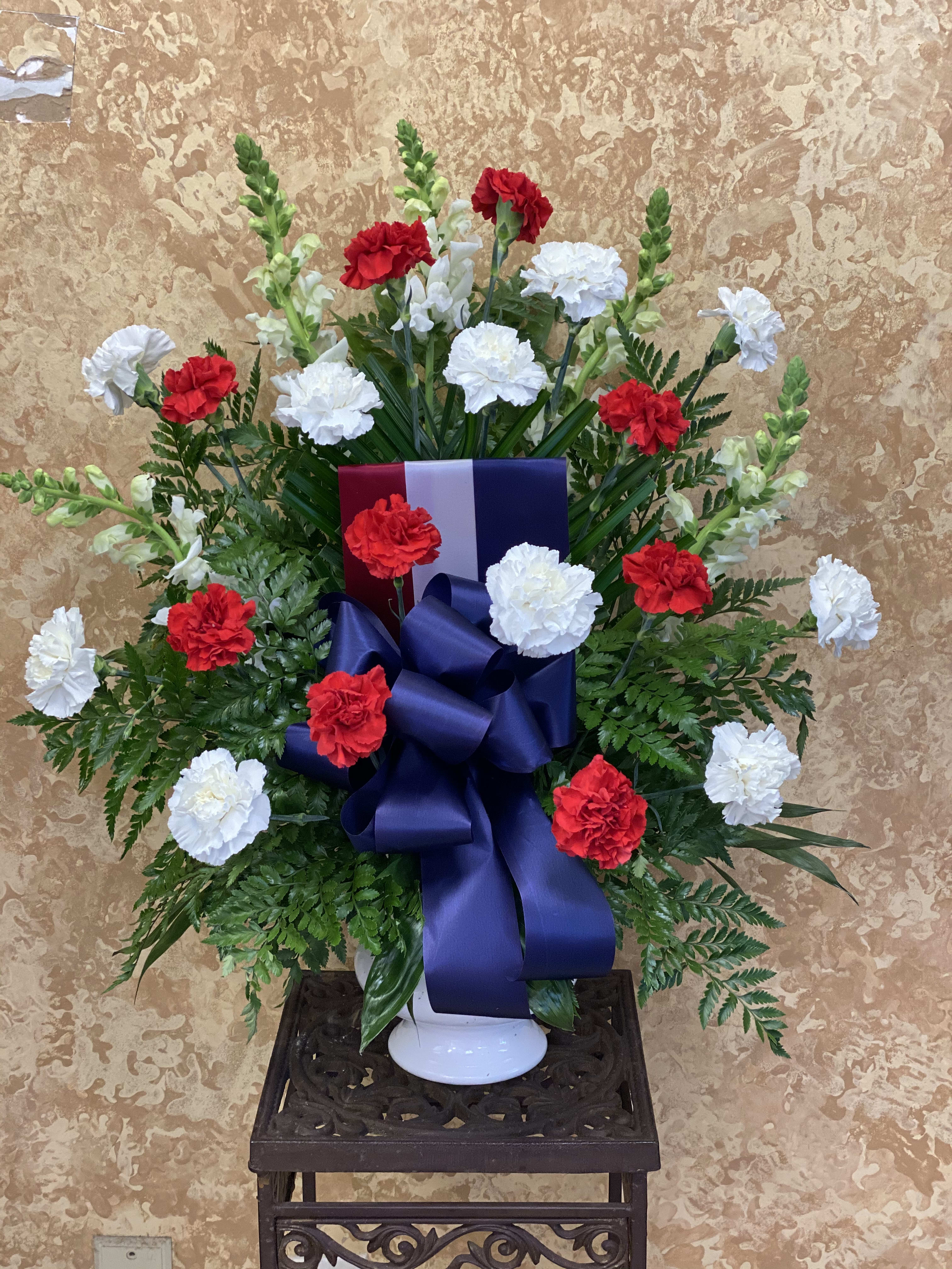 Red and white carnations in a white vase with a large blue ribbon