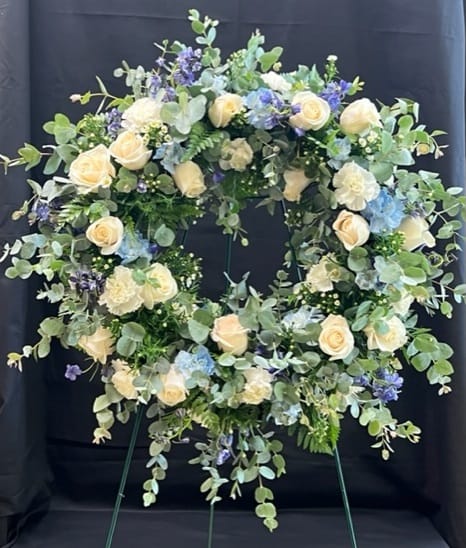 Circular floral wreath with cream roses and blue flowers on an easel