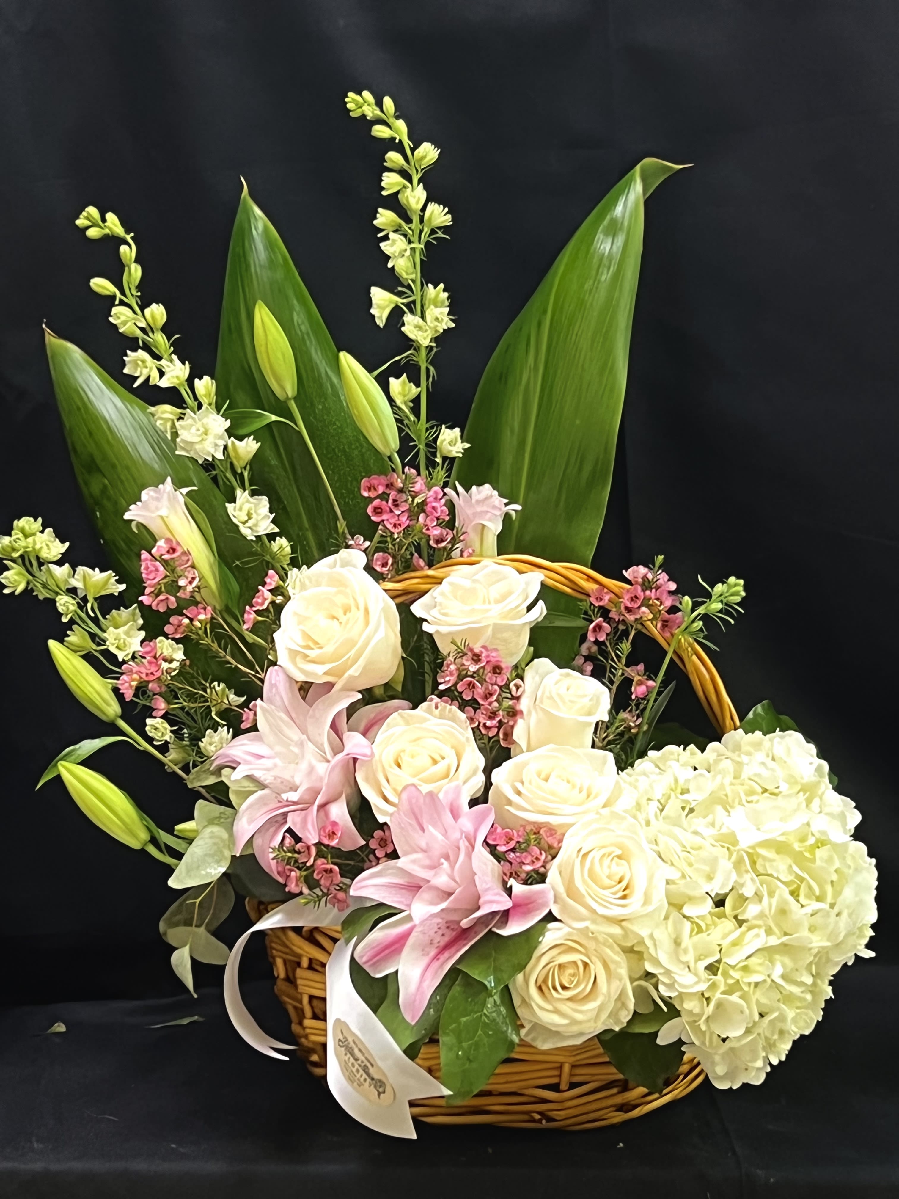 Basket arrangement of cream roses, pink lilies, and white hydrangea