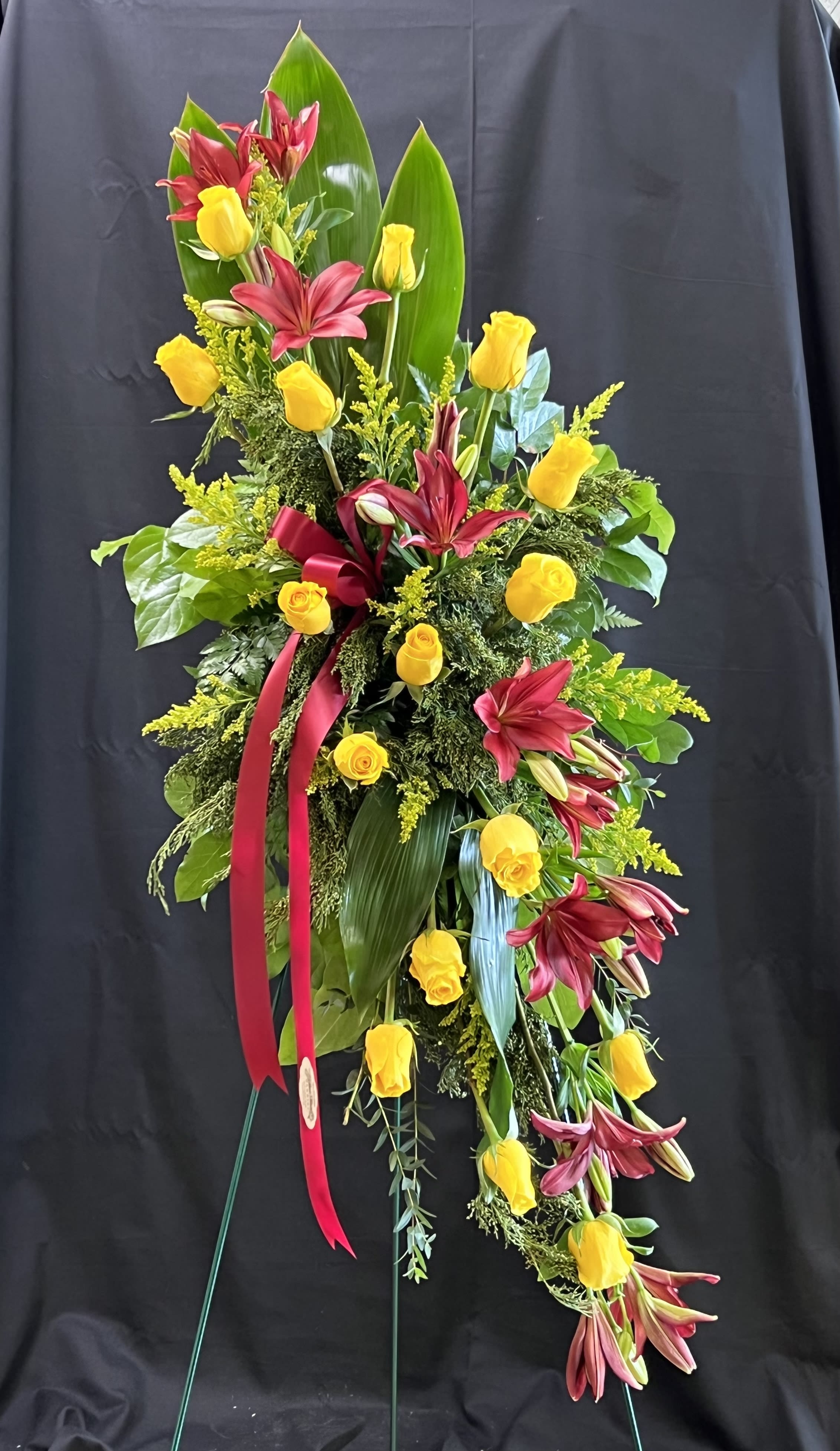Tall floral spray with yellow roses and burgundy lilies on a stand