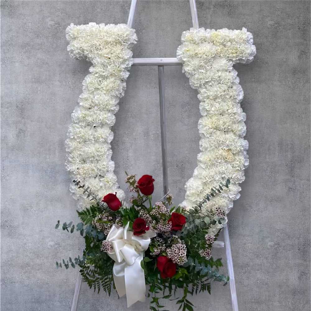 White floral standing spray with red roses and a white ribbon