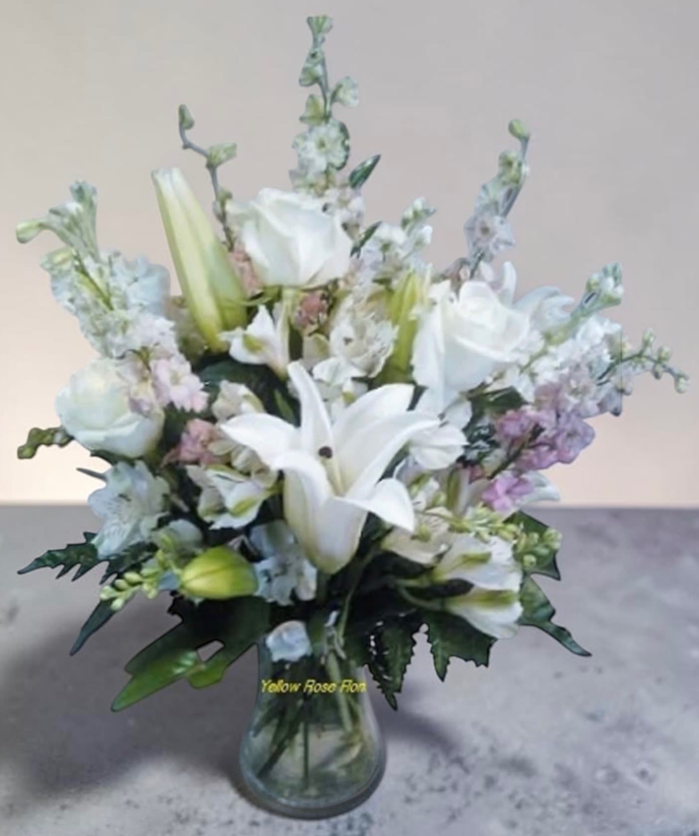 White Lily Enchantment - This lovely arrangement consist of white lilies, white roses, alstroemeria greenery and a touch of ever so light pink larksburg gathered in a clear glass vase. 
