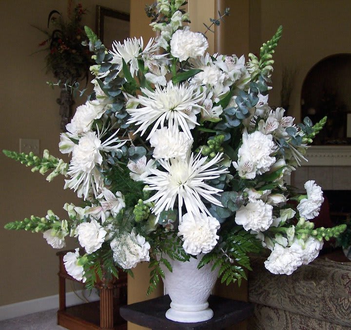 White floral arrangement in a white vase with spiky blooms and carnations