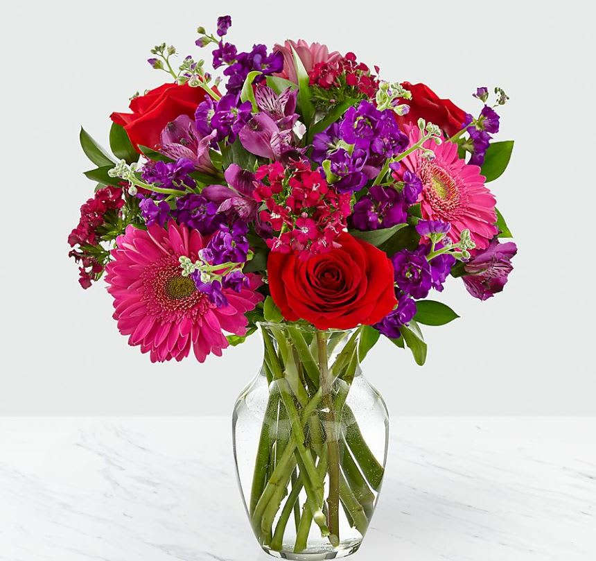 Lucky in Love Bouquet - VASE INCLUDED - Picked fresh from the farm, our Lucky in Love Bouquet creates the perfect Valentine's Day gift! Hand gathered at select floral farms, this bouquet brings together bright pinks, eye-catching purples, and bold reds to create a Valentine display that would make Cupid proud. Picked fresh for you, this flower bouquet is a wonderful gift to send to your favorite friends, family, or special someone in honor of this coming February 14th. Bouquet includes: red roses, hot pink gerbera daisies, purple gilly flower, purple Peruvian Lilies, hot pink dianthus, and lush greens with a glass vase. Approx. 14"H x 13"W.  