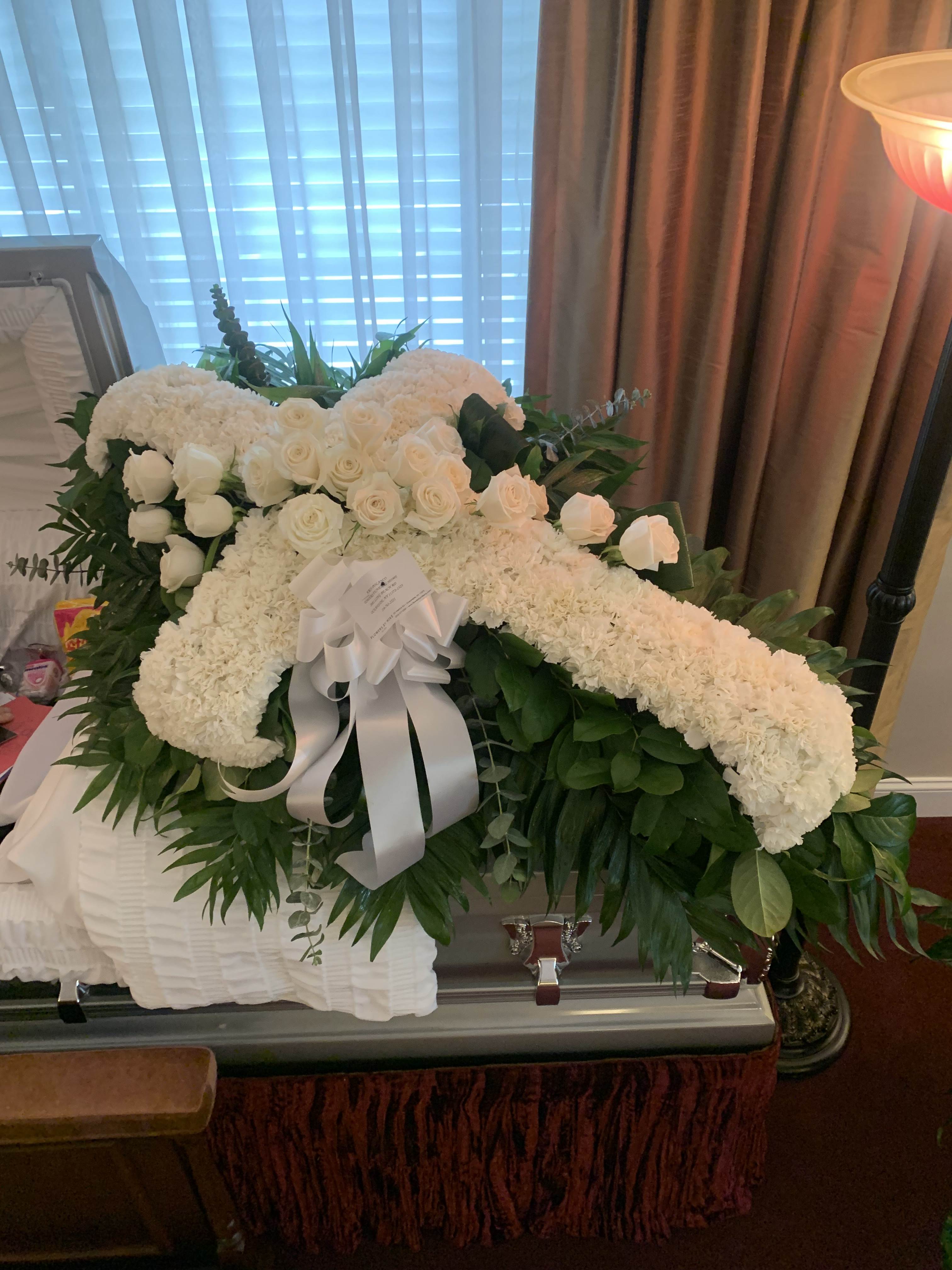 White roses and hydrangeas arranged on a casket with a white ribbon