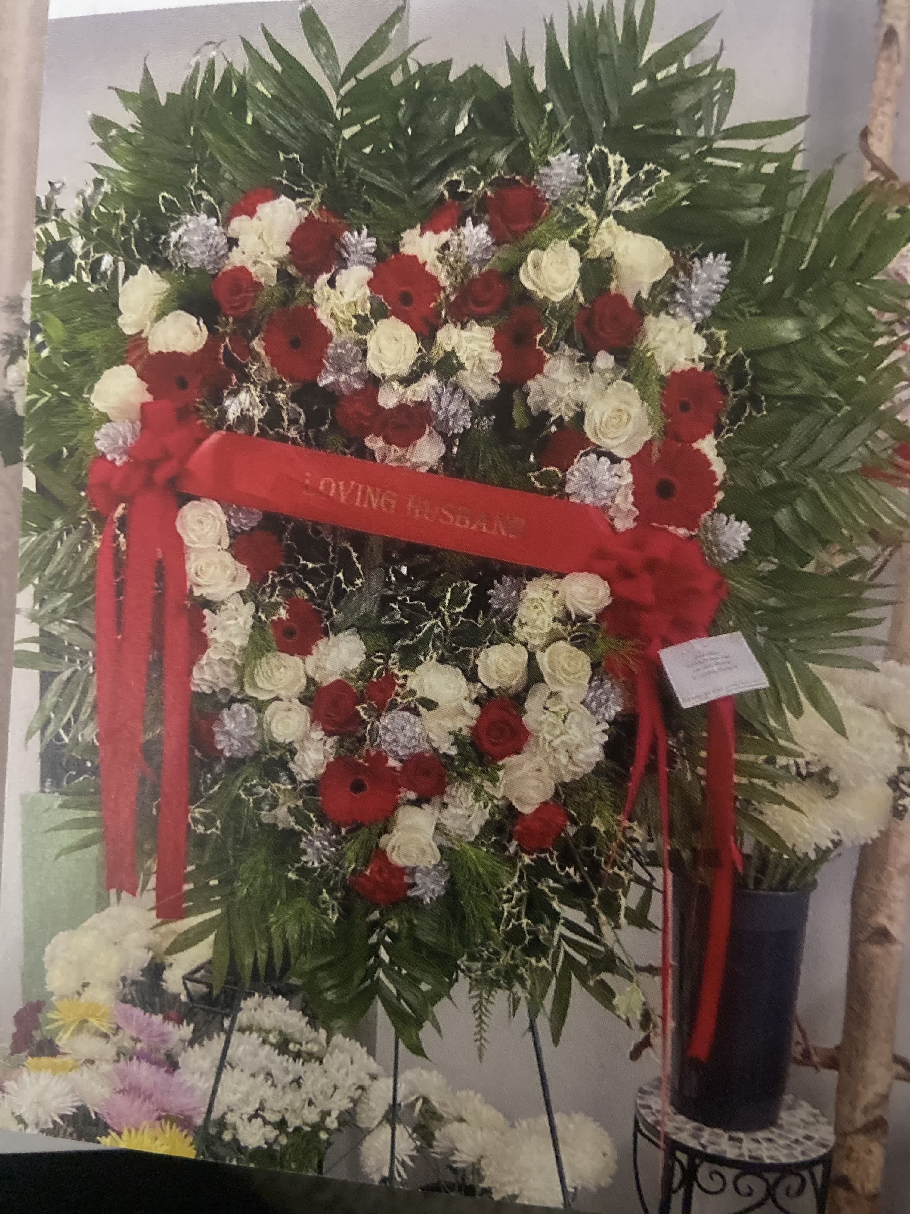 Heart-shaped funeral wreath with red and white flowers and a red ribbon
