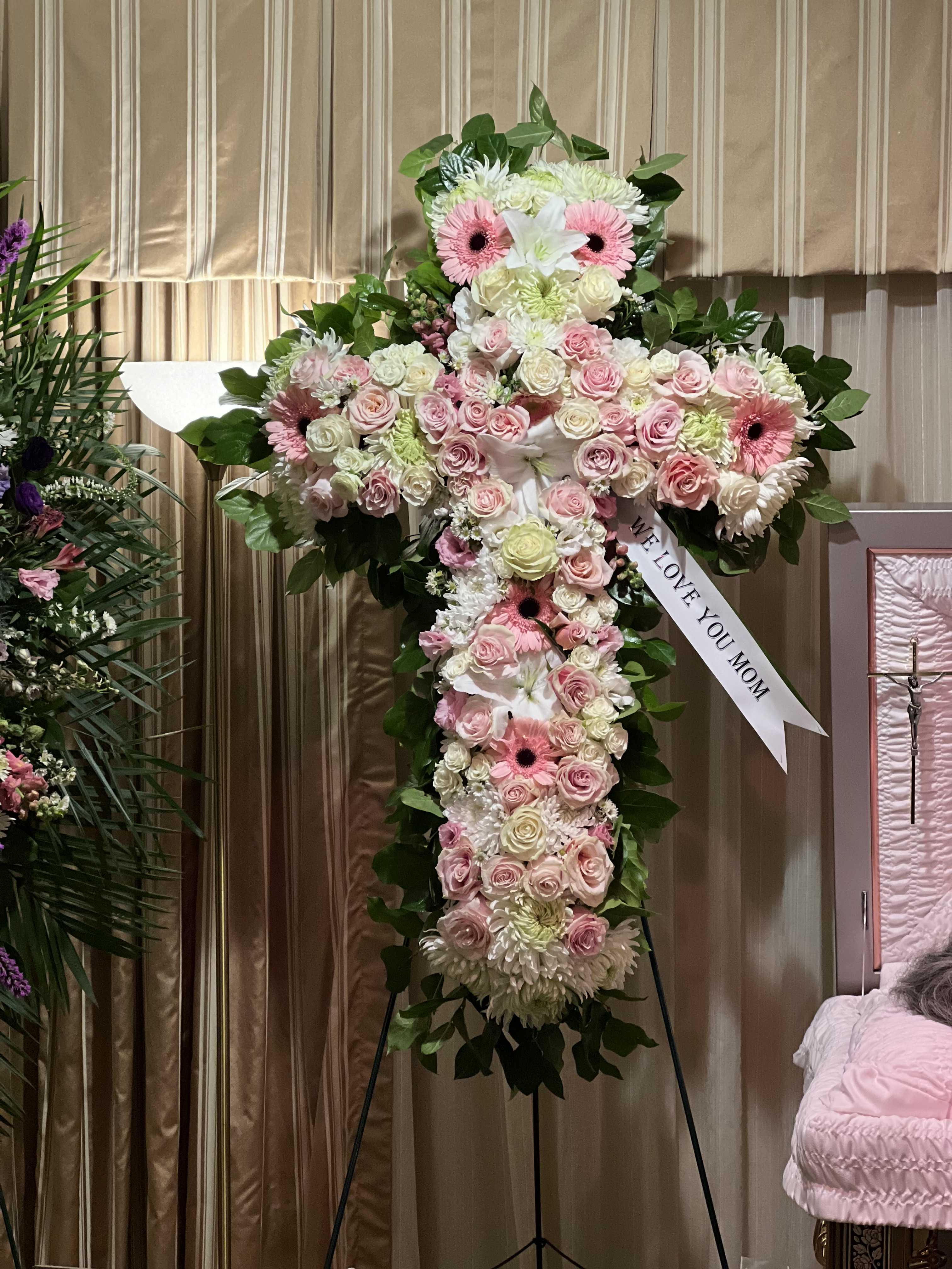 Large cross-shaped floral tribute with pink and white flowers on an easel