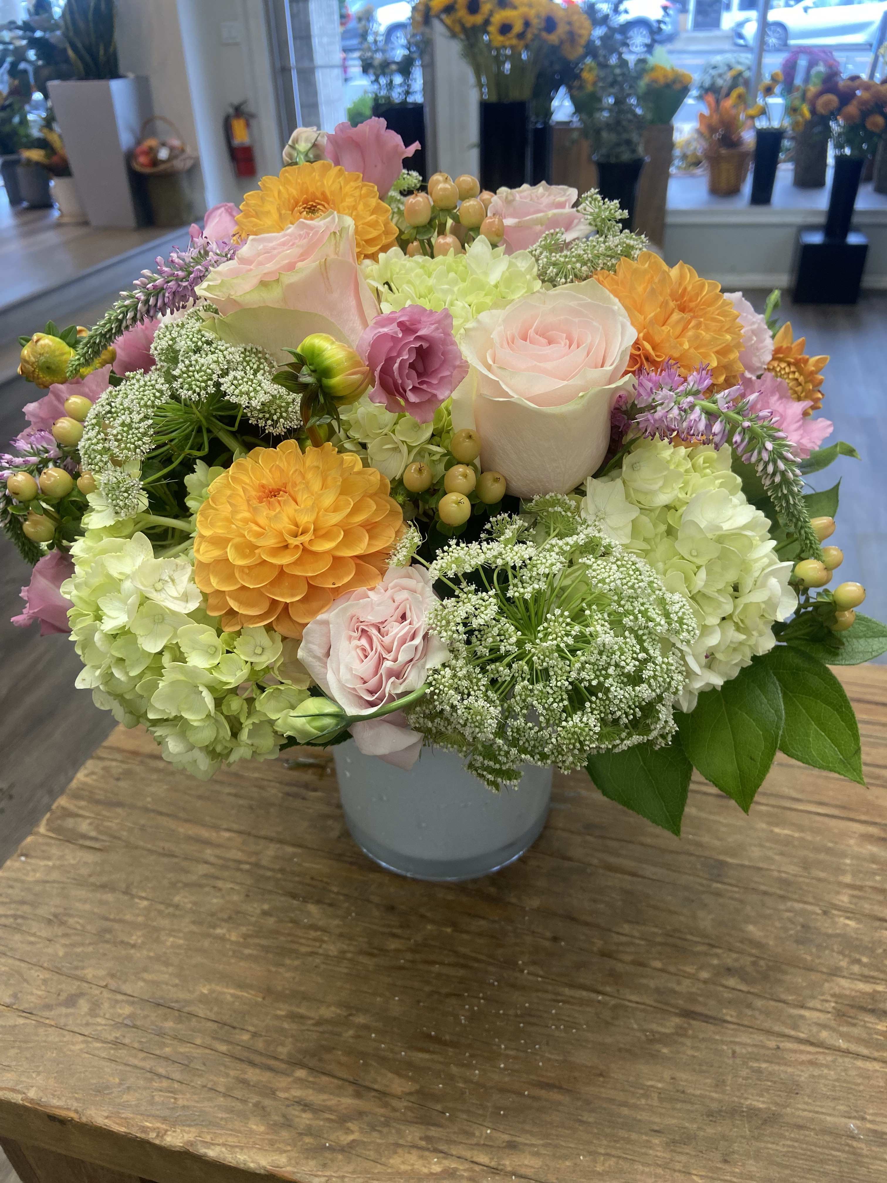 Mixed pastel bouquet in a gray vase with roses, hydrangeas, and orange blooms