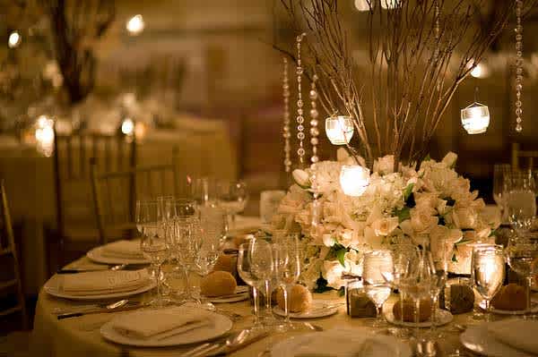 White floral centerpiece with hanging candle lights on a banquet table