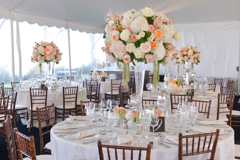 Tall pastel floral centerpieces on round banquet tables in a tented reception