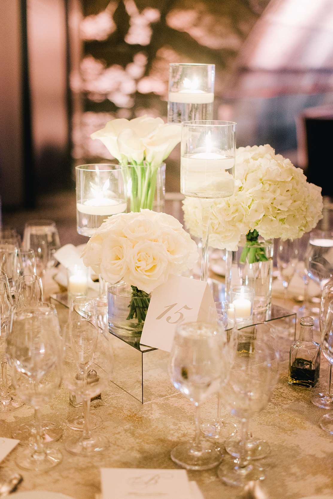 White floral centerpieces with candles in glass cylinders on a table