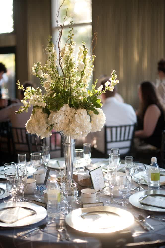 Tall white floral centerpiece in a silver vase on a set dining table