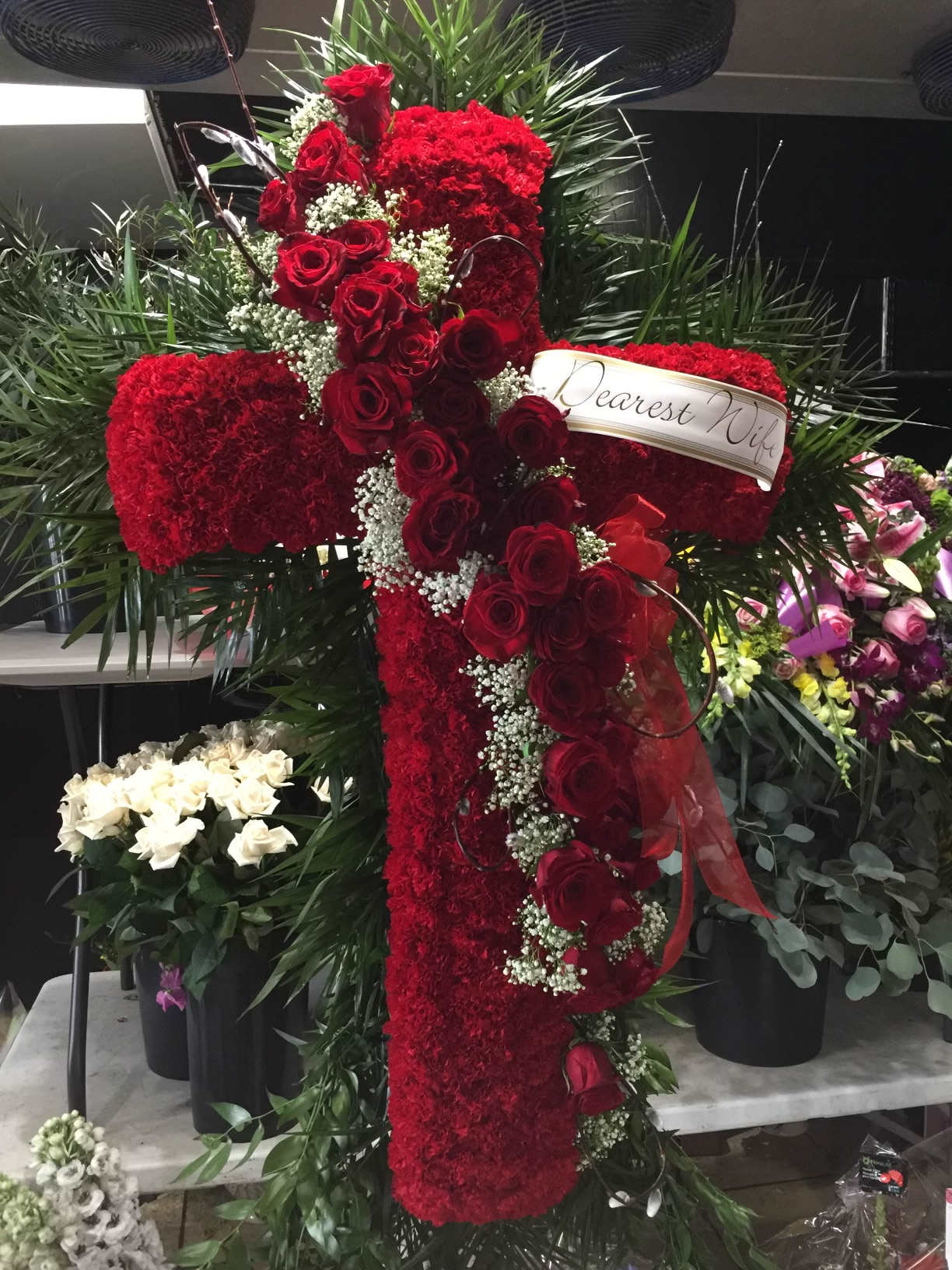 Red rose and carnation cross-shaped funeral spray with a ribbon