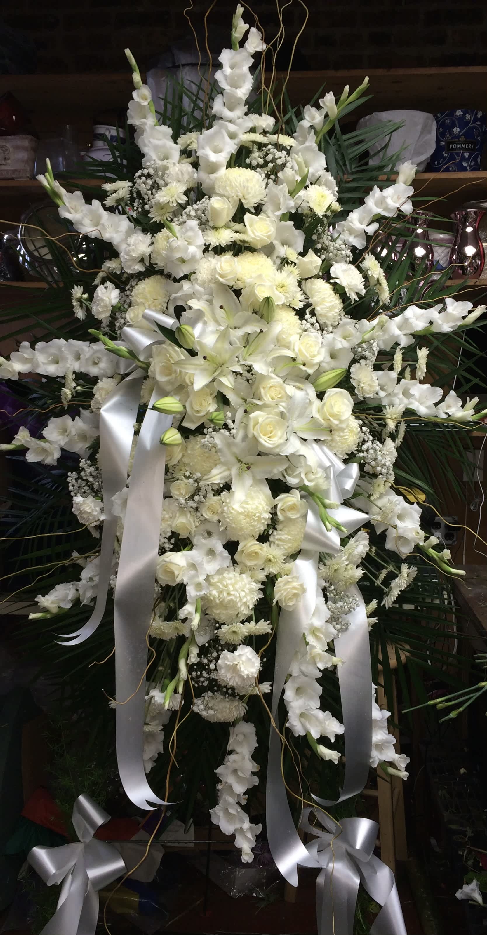 Large white funeral spray with lilies, roses, and ribbons