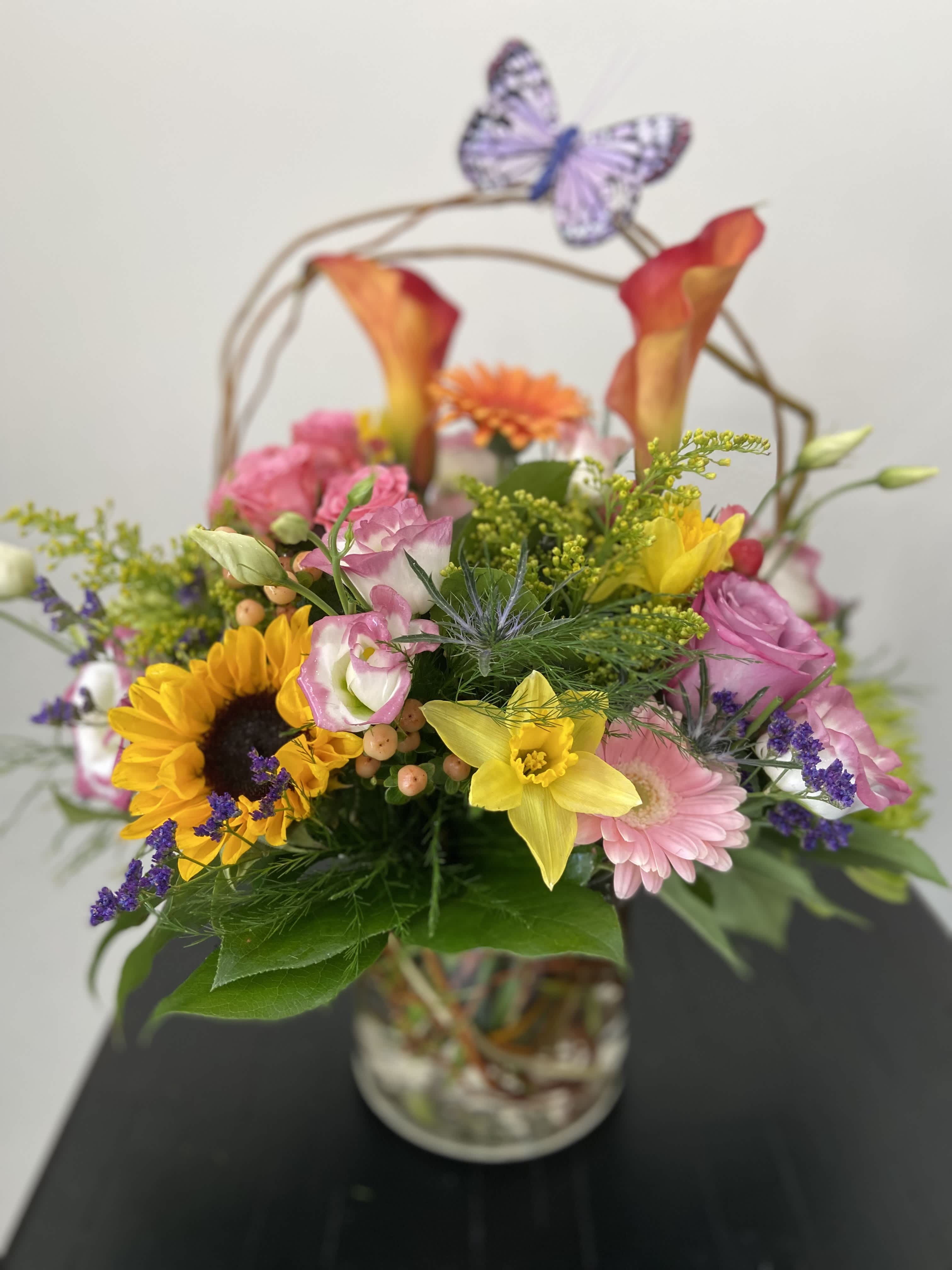 Mixed bouquet in a glass vase with sunflowers, pink blooms, and calla lilies