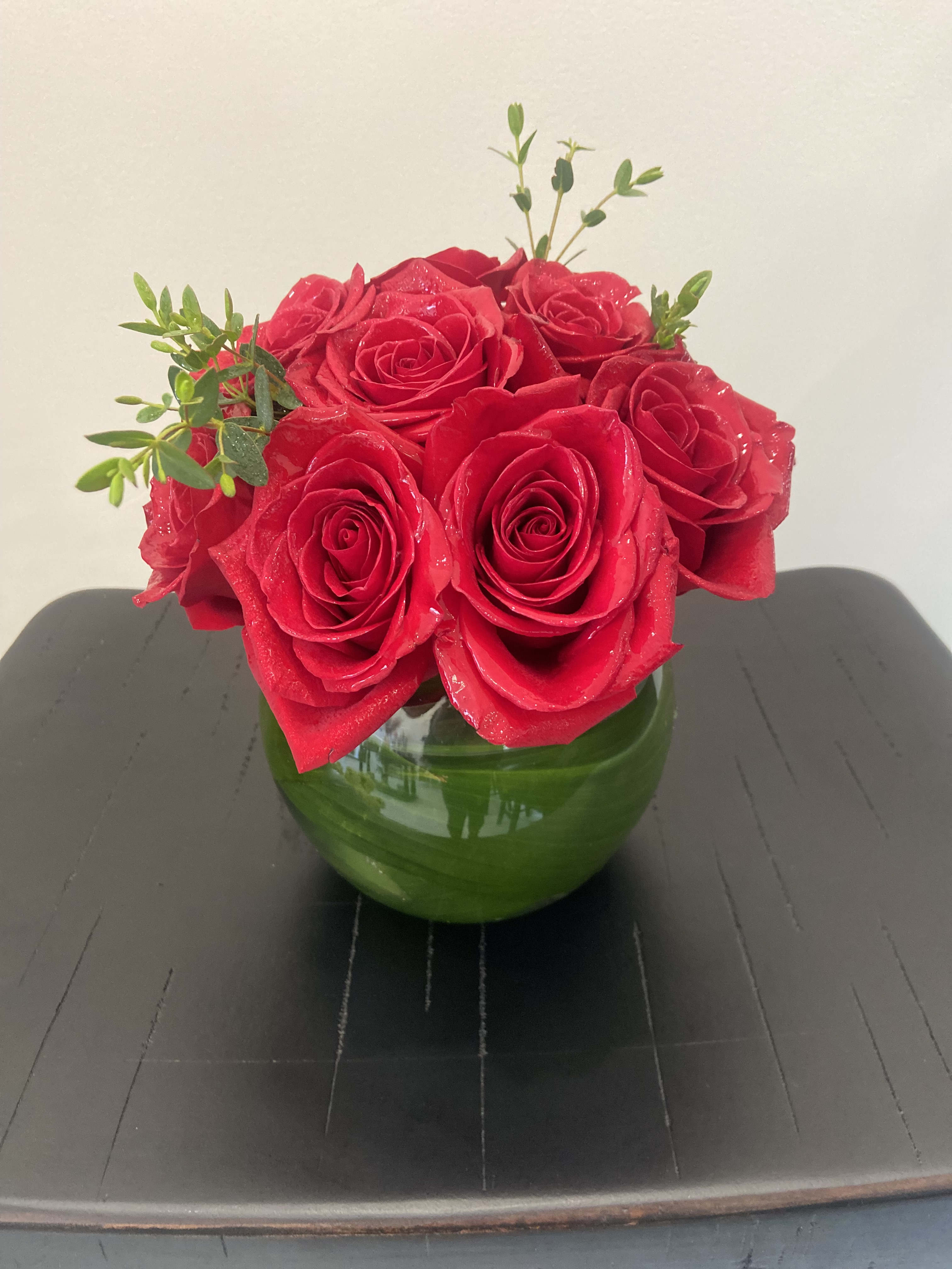 Red roses arranged in a green glass vase