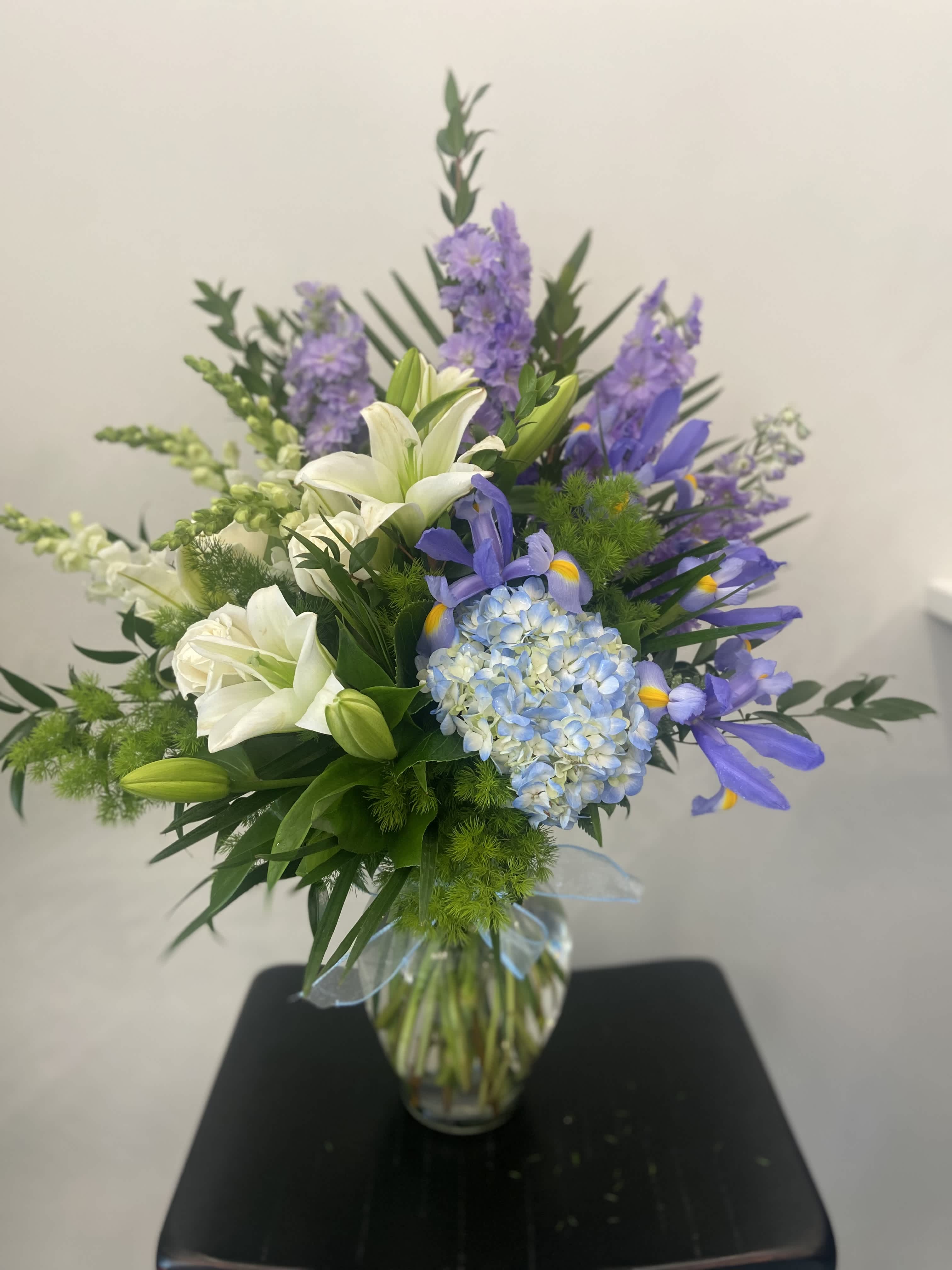 White lilies and blue-purple flowers in a glass vase
