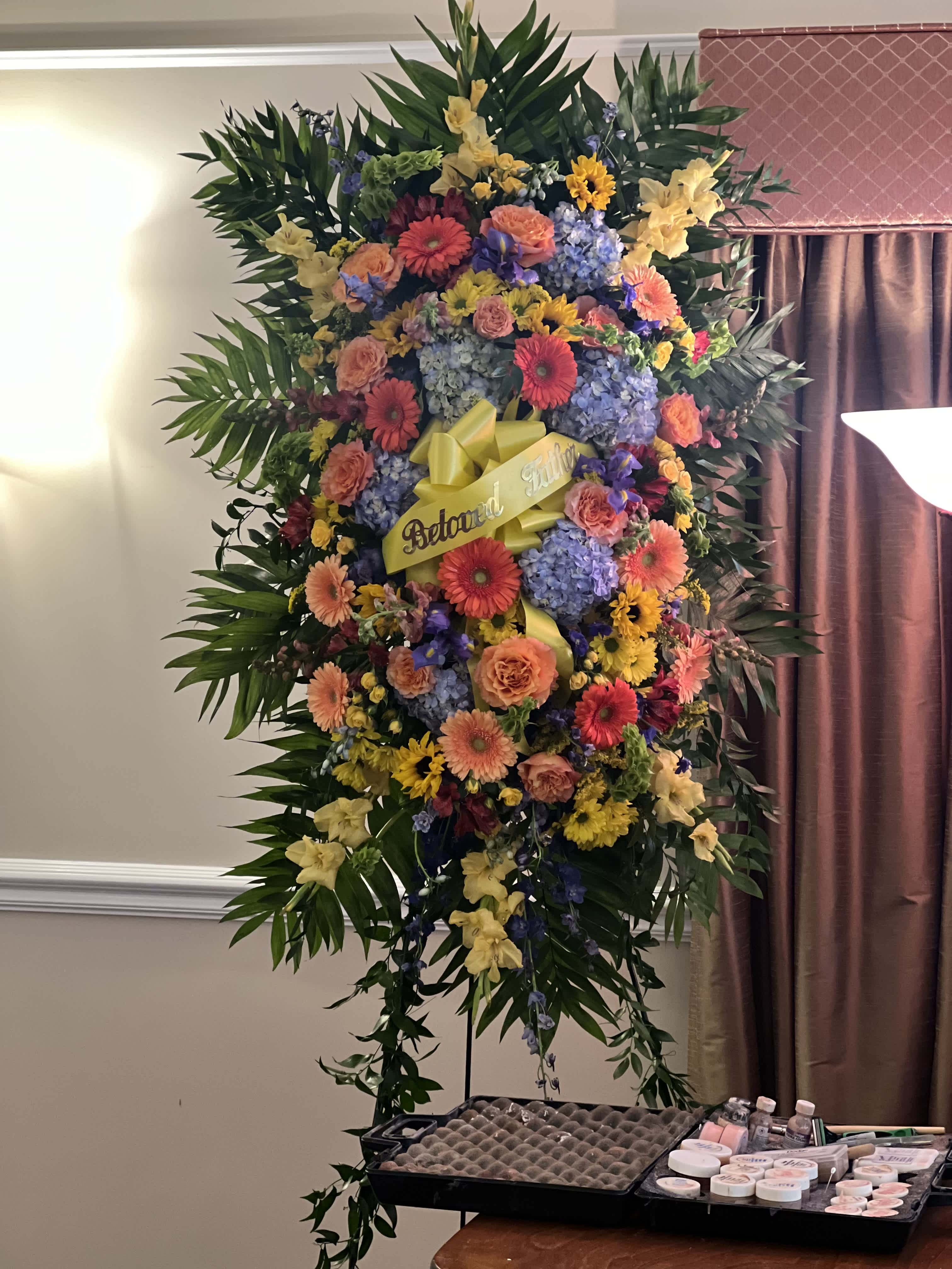 Large standing floral spray with a yellow ribbon and mixed blooms