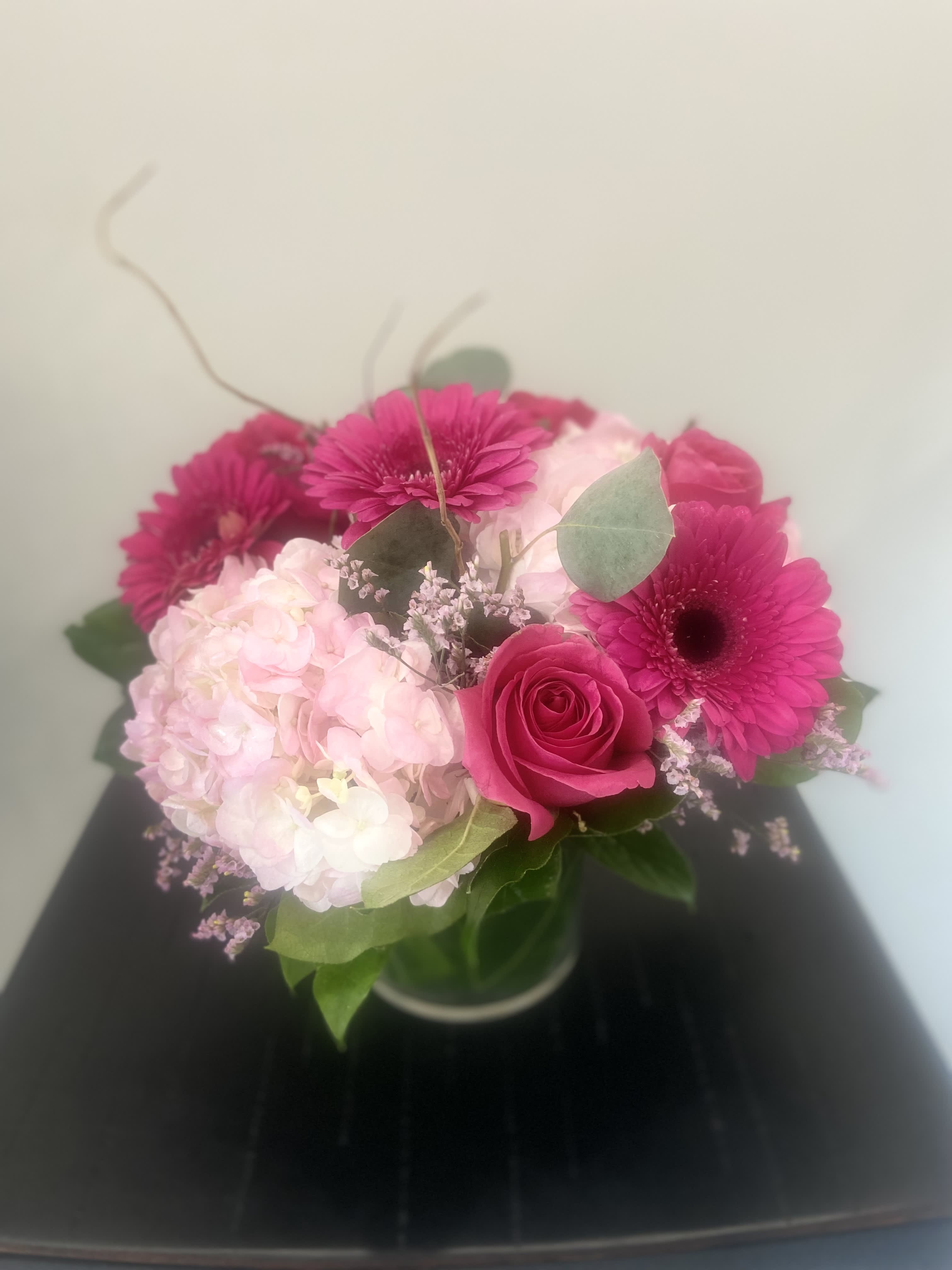 Pink gerbera daisies, a rose, and pale hydrangea in a glass vase