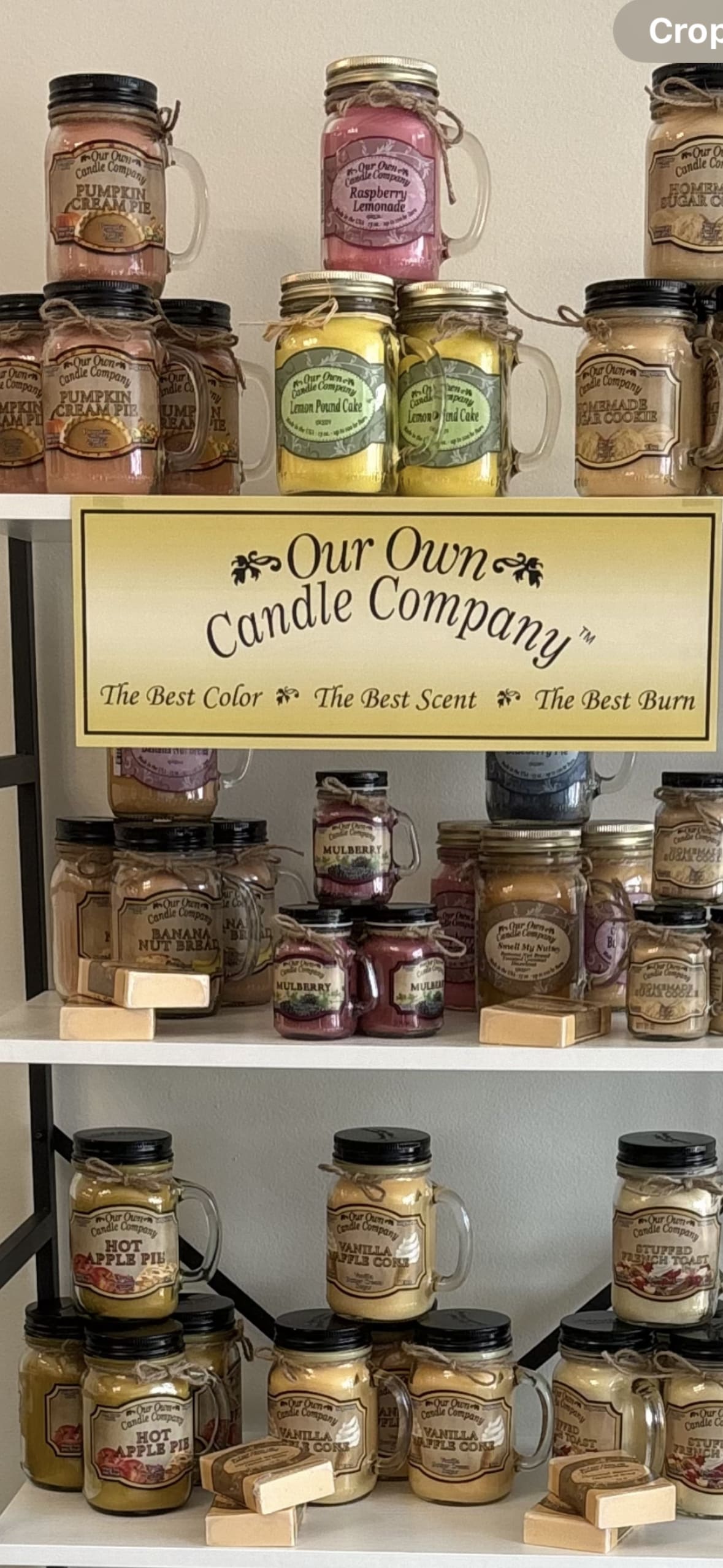 Shelf display of scented candles in mason jars with a company sign.