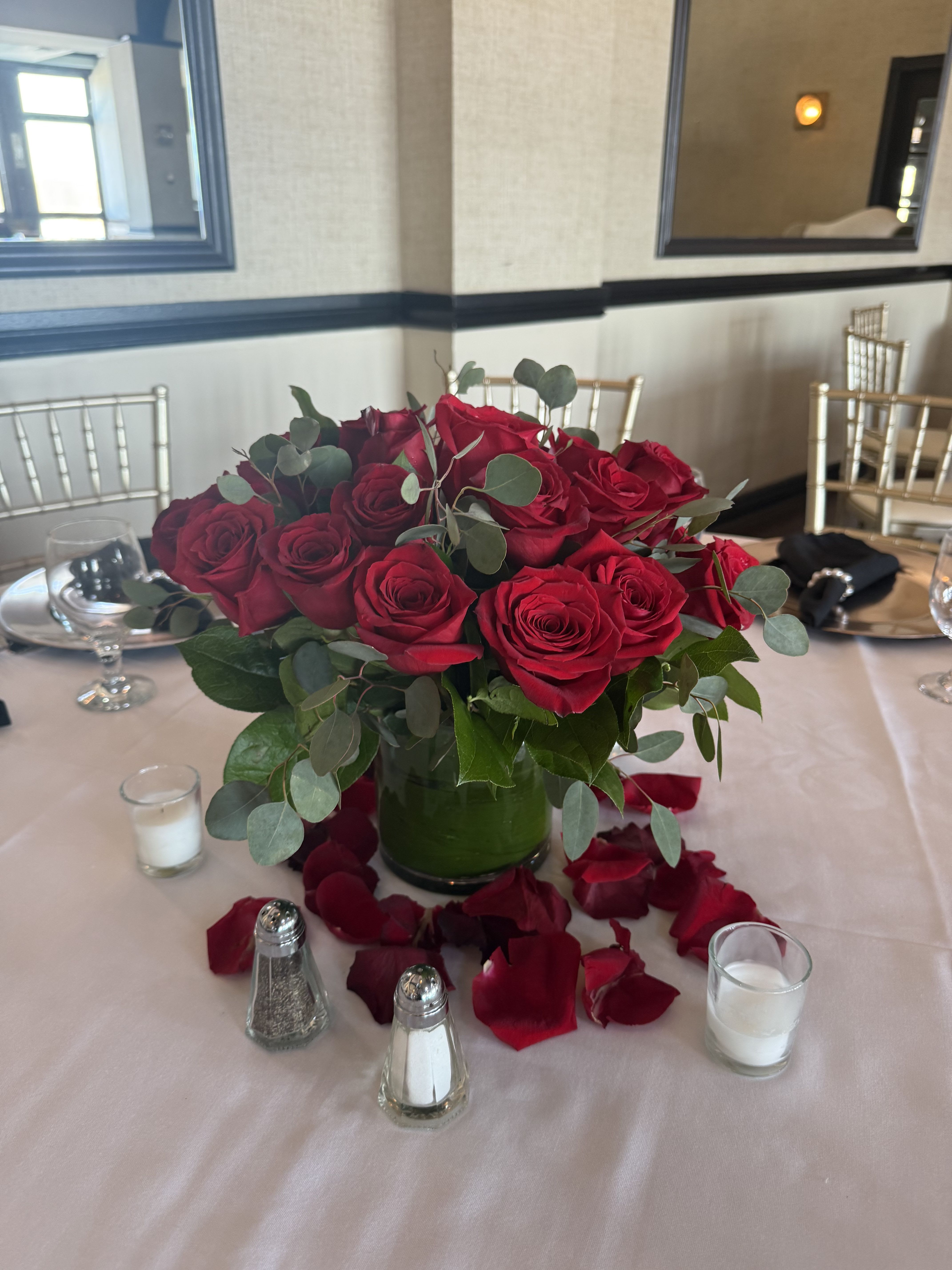 Red rose centerpiece in a glass vase with scattered petals