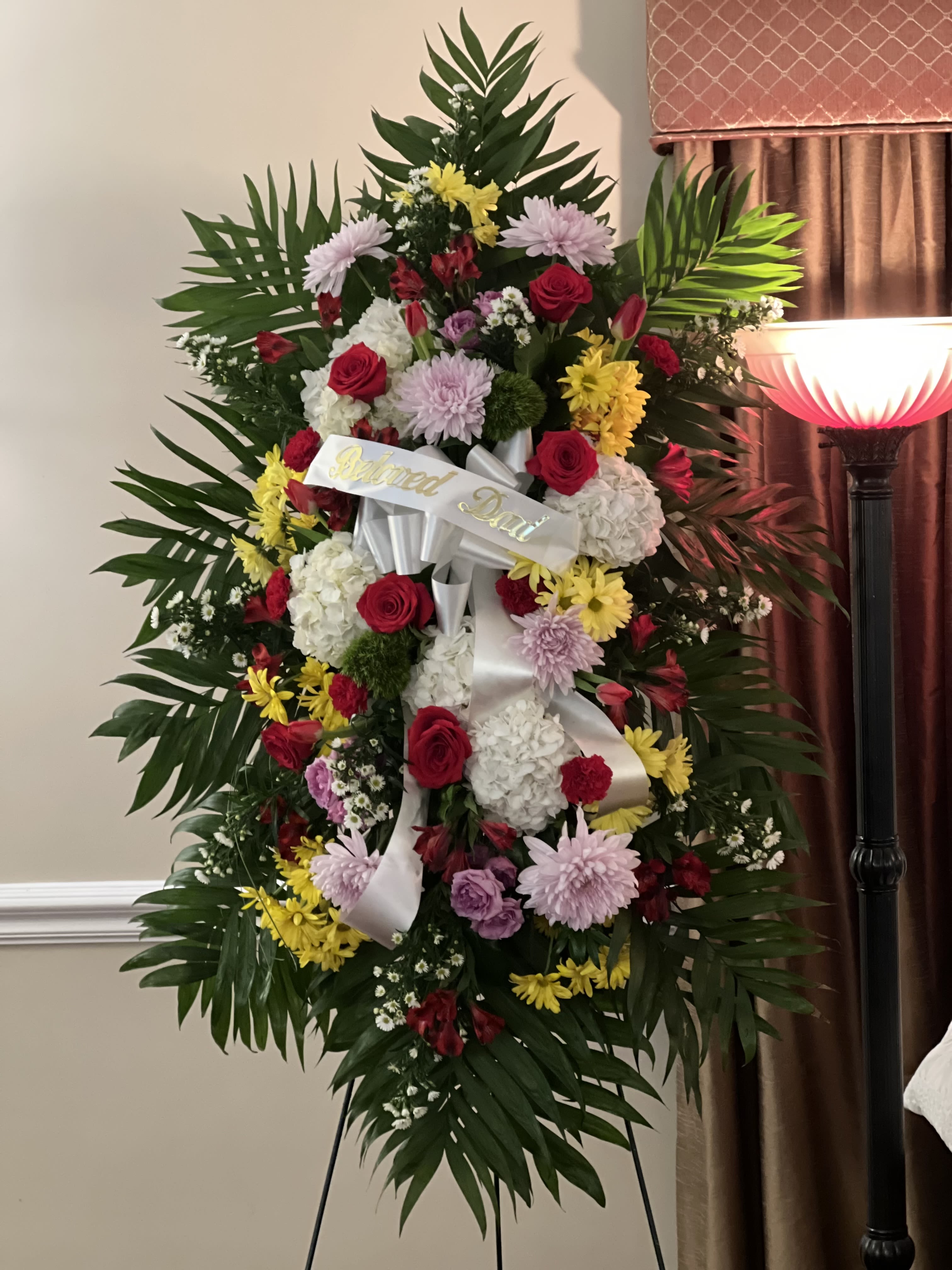 Standing funeral wreath with red, pink, yellow, and white flowers