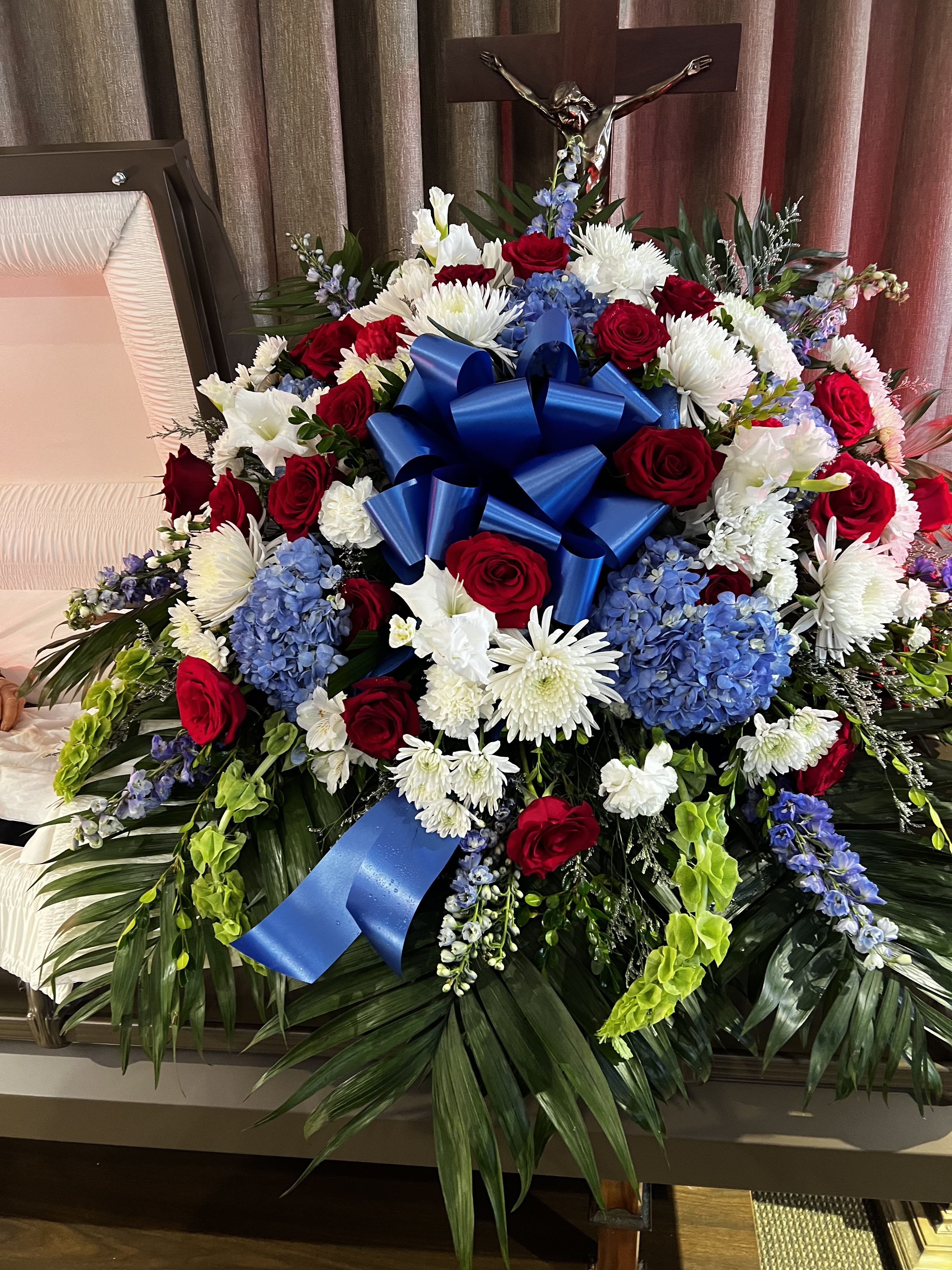 Large funeral spray with red roses, white chrysanthemums, and blue ribbon