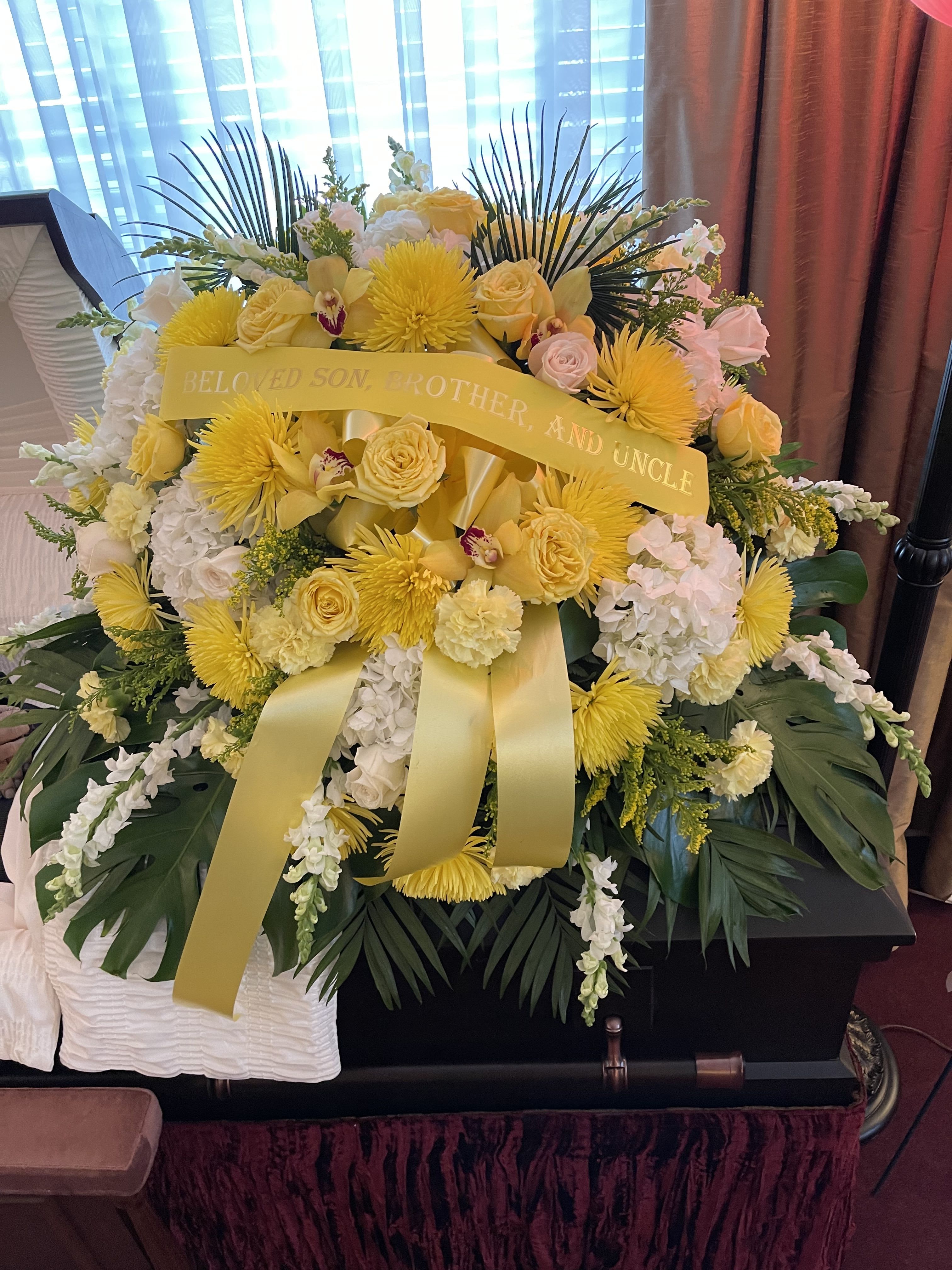 Yellow and white funeral spray with ribbon on a casket