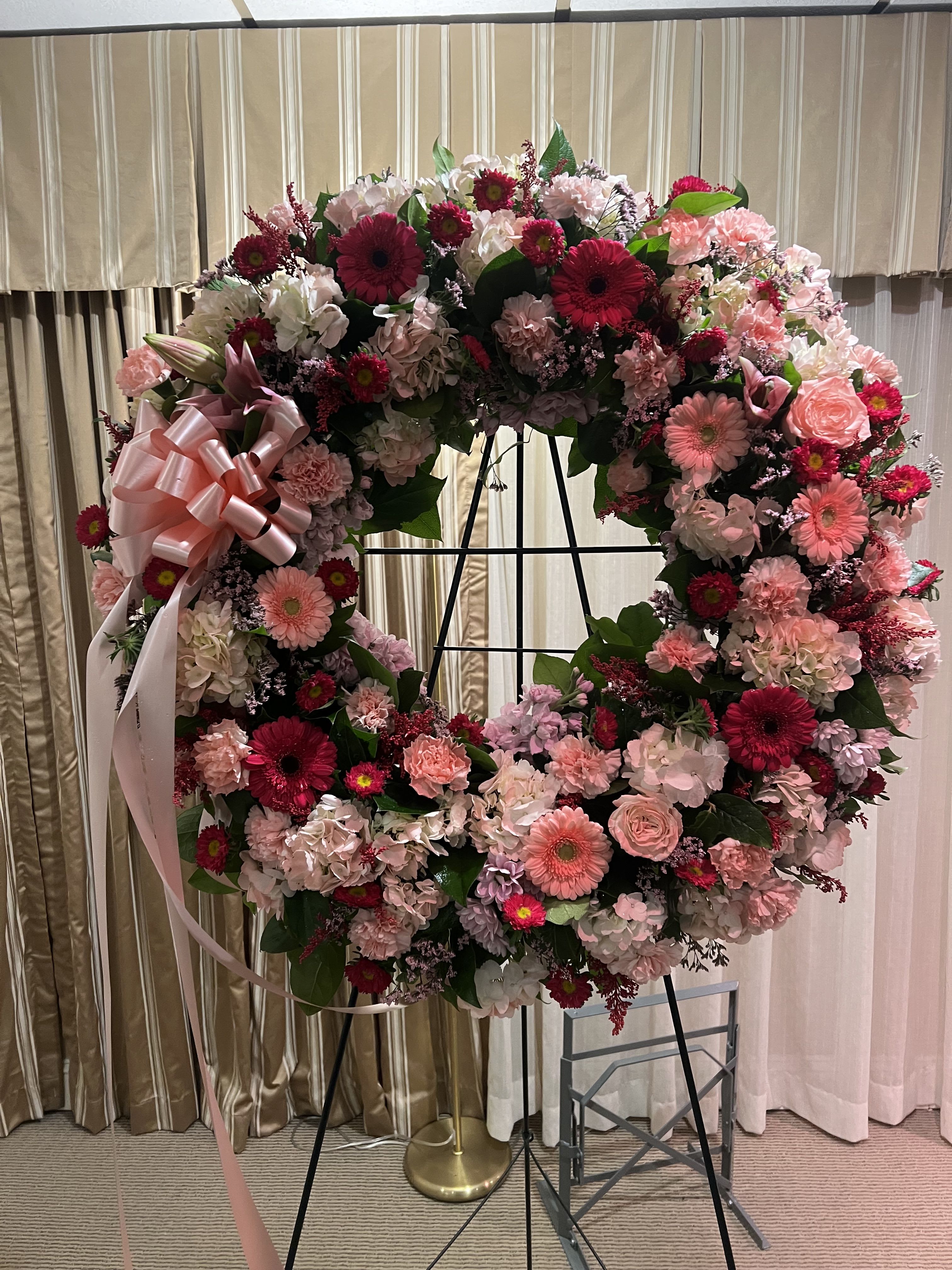 Large pink and white floral wreath on a stand with a ribbon bow