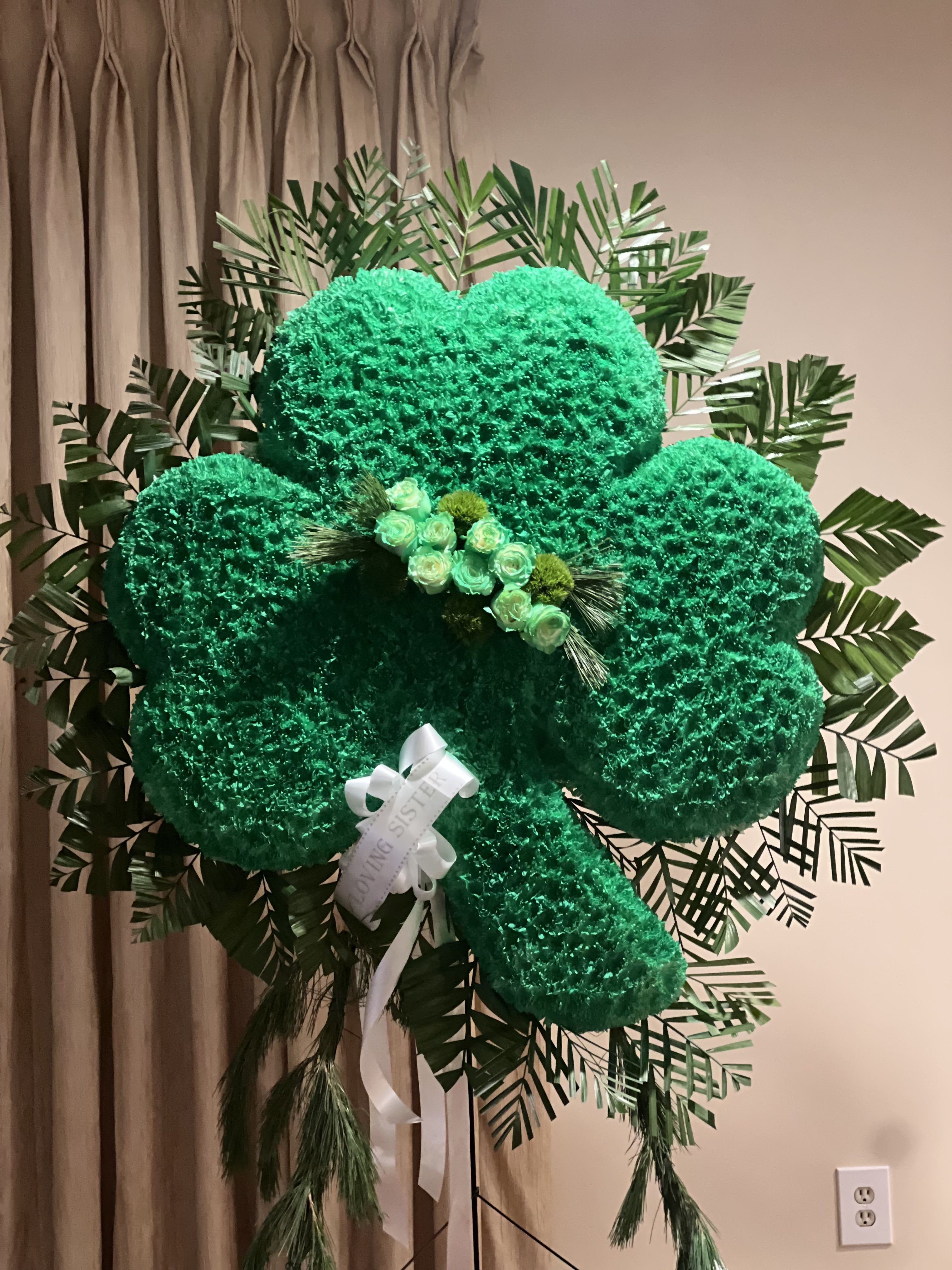 Large green floral clover display with a white ribbon and small roses